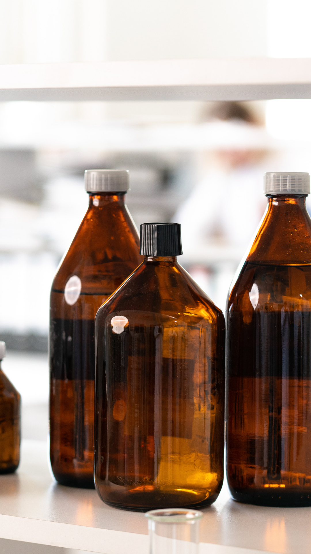 Three amber glass bottles with white and black caps on a white lab shelf.