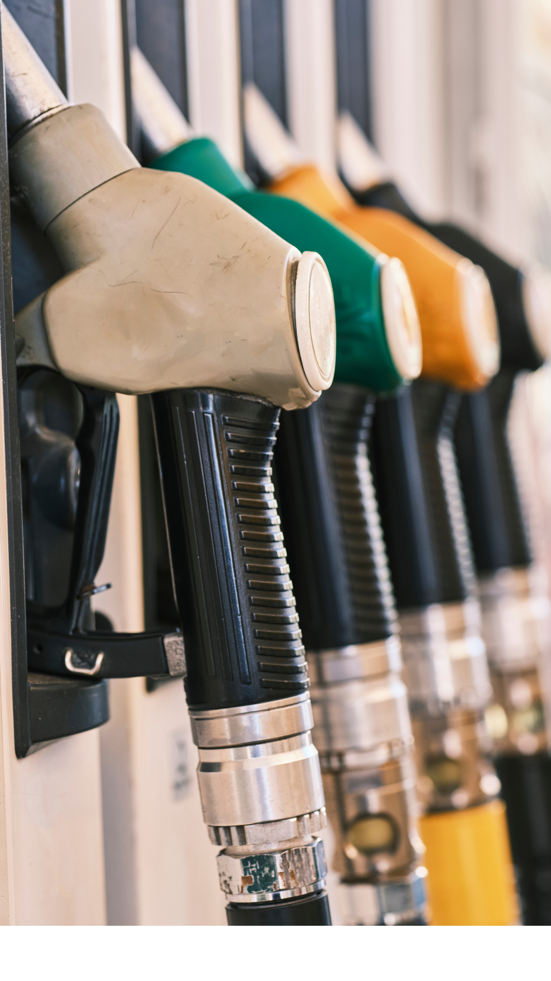 A row of gas pump nozzles in beige, green, orange, and black colors at a gas station.