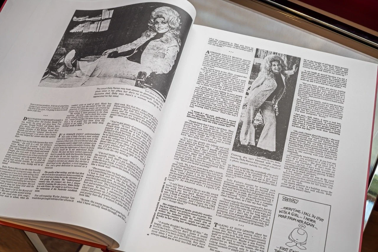 Open magazine featuring black and white photos of a woman with curly hair, wearing a jacket and pants, and a comic strip in the corner.
