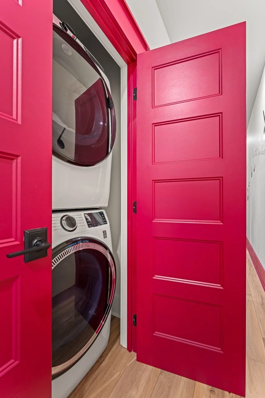 A stacked washer and dryer inside a small closet with a pink door.
