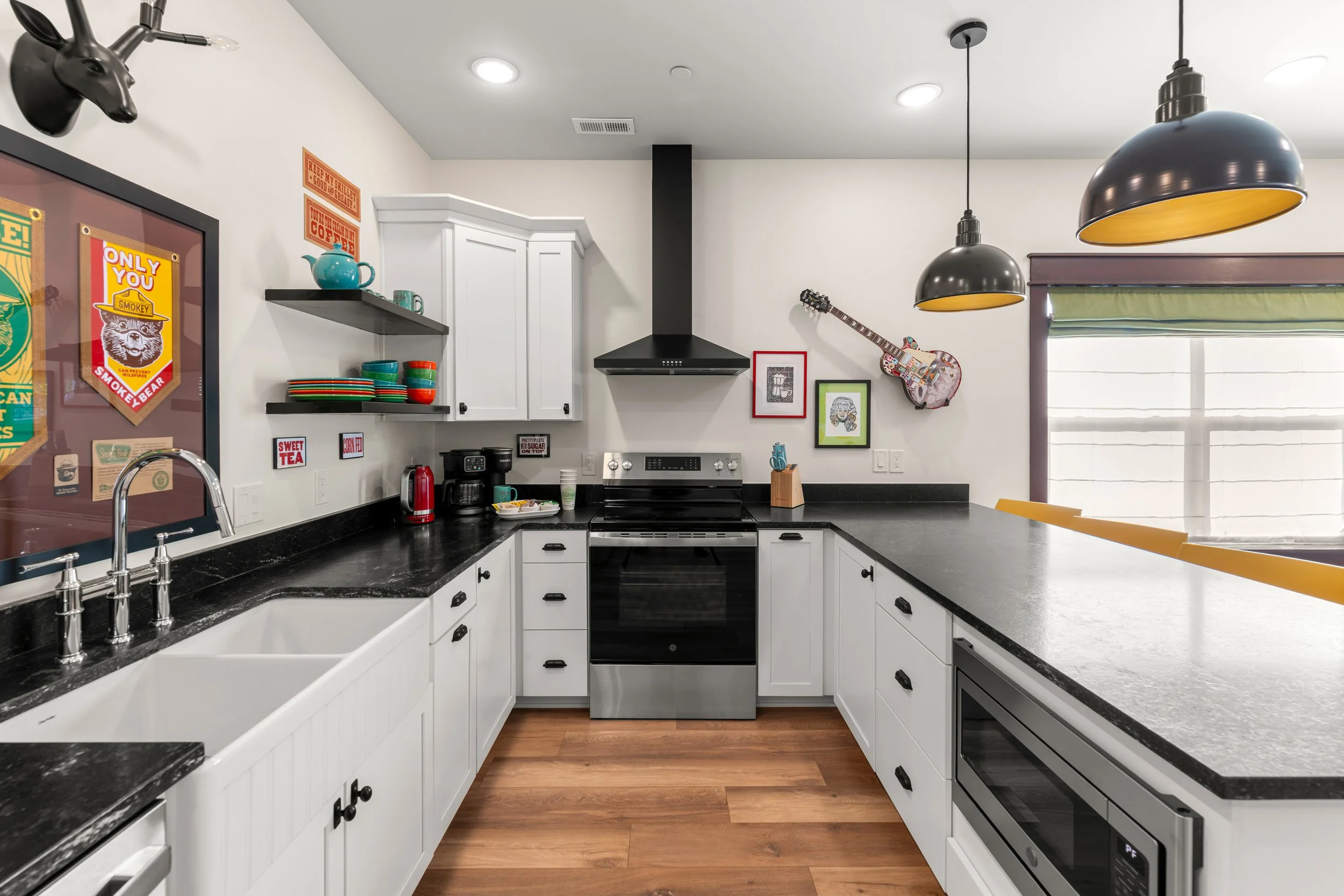 Modern kitchen with white cabinets, black countertops, black and yellow pendant lights, and various decorative items on the walls and shelves.