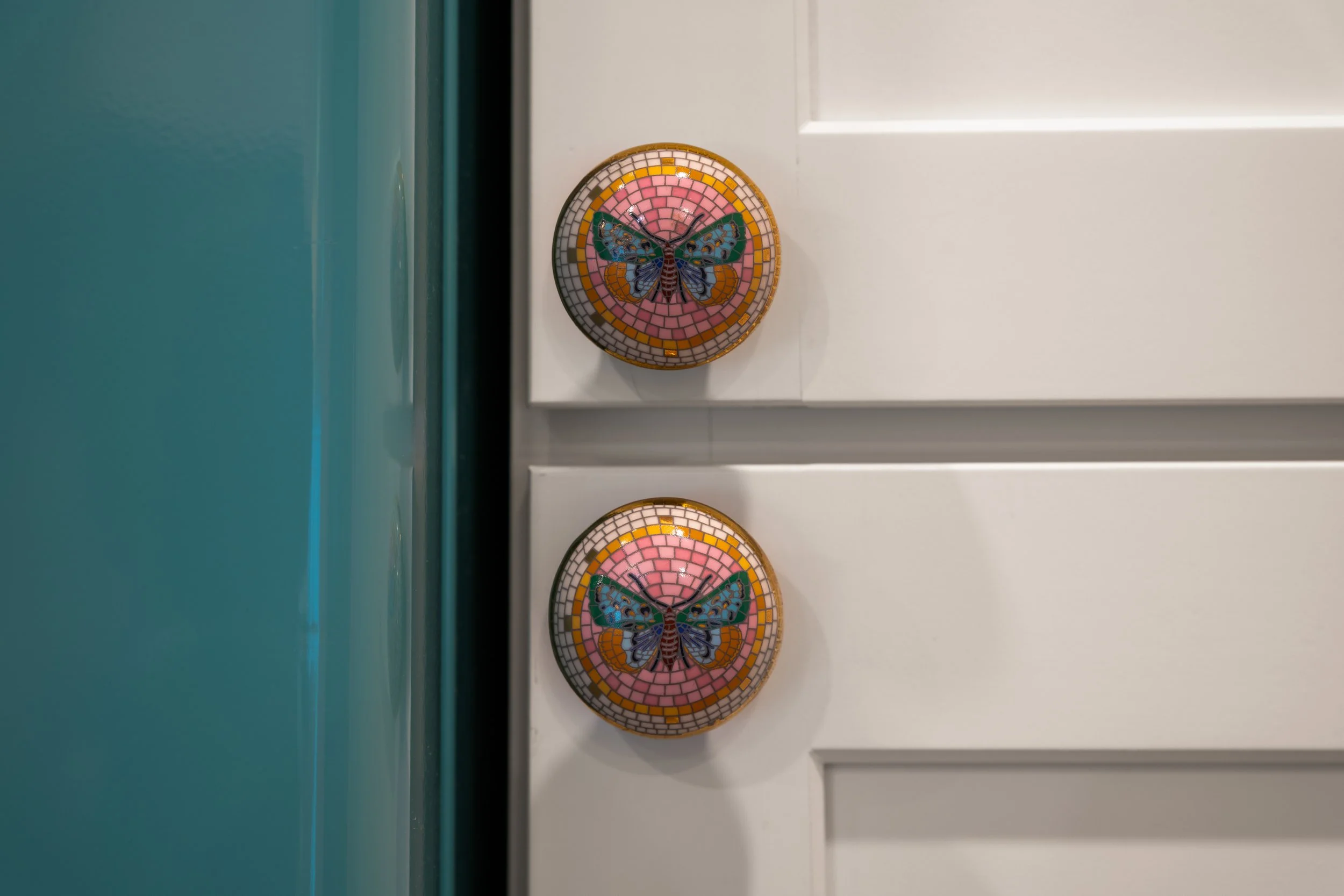 Two round mosaic coasters with butterfly and dragonfly designs on a white surface, with a teal background visible to the left.