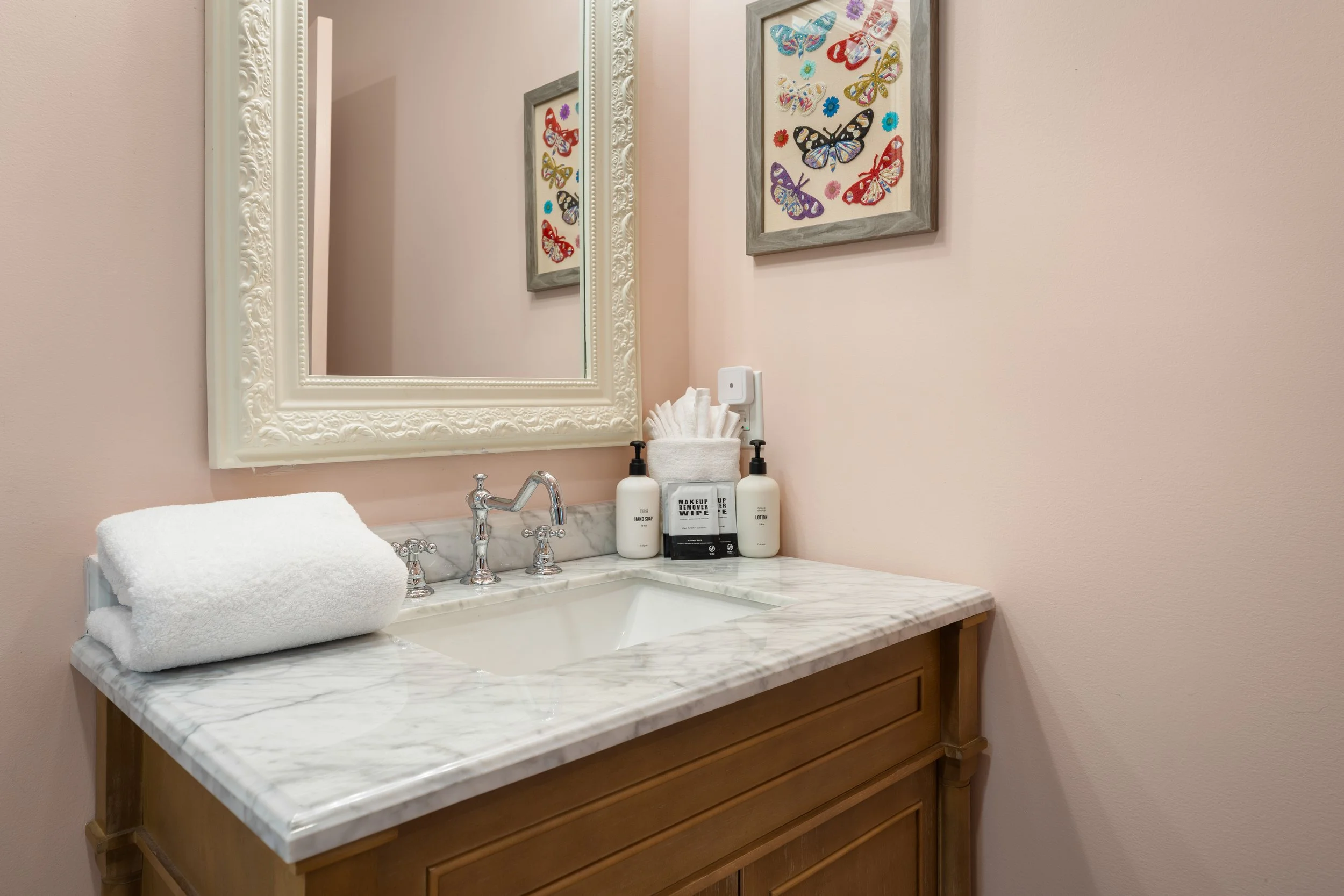 Bathroom vanity with a marble countertop, a framed mirror, a towel rolled on the counter, and decorative butterfly art on the wall.