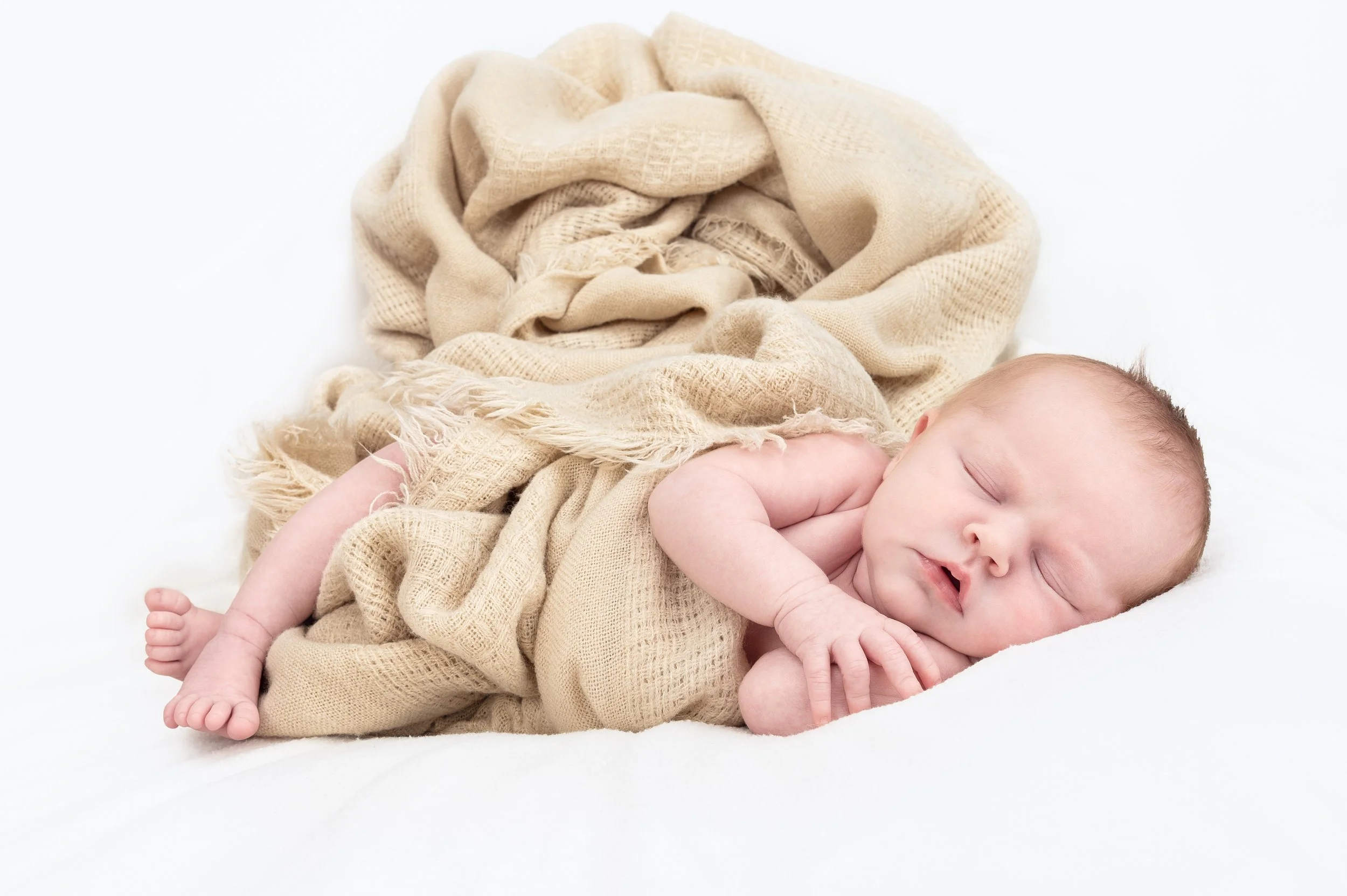 En nyfødt baby ligger på en hvit seng, kledd i brunt, ullsokker, og ser mot kamera.