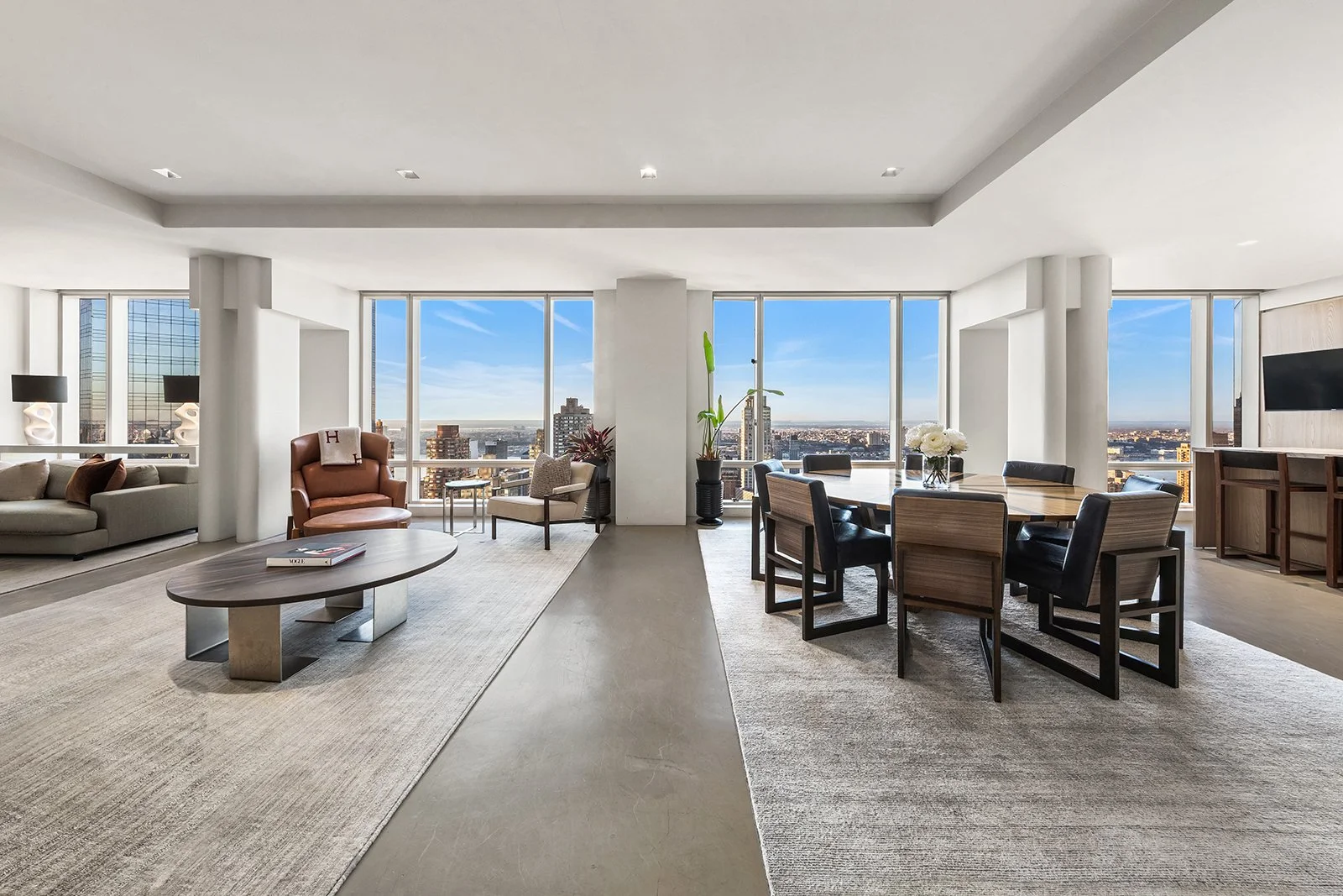 Modern high-rise apartment living room with large windows overlooking city skyline, featuring a dining table with six chairs, a sofa, armchairs, and decorative lamps.