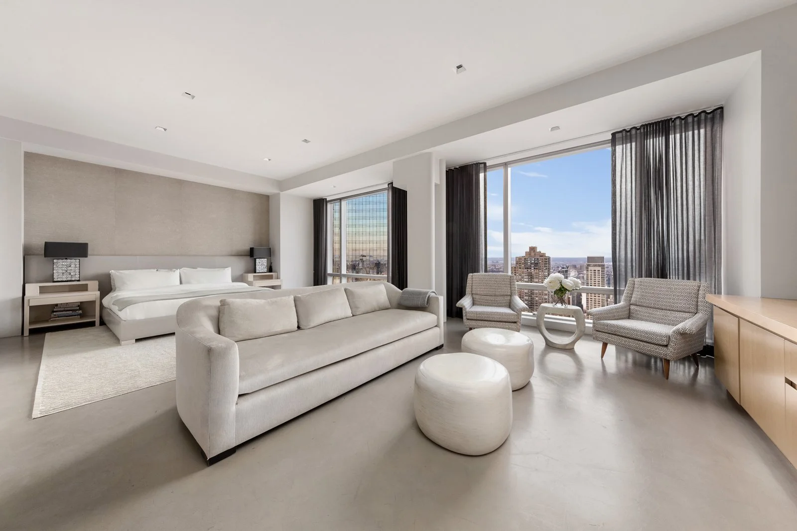 Modern hotel living room with large windows, white sofa, armchairs, and city view.
