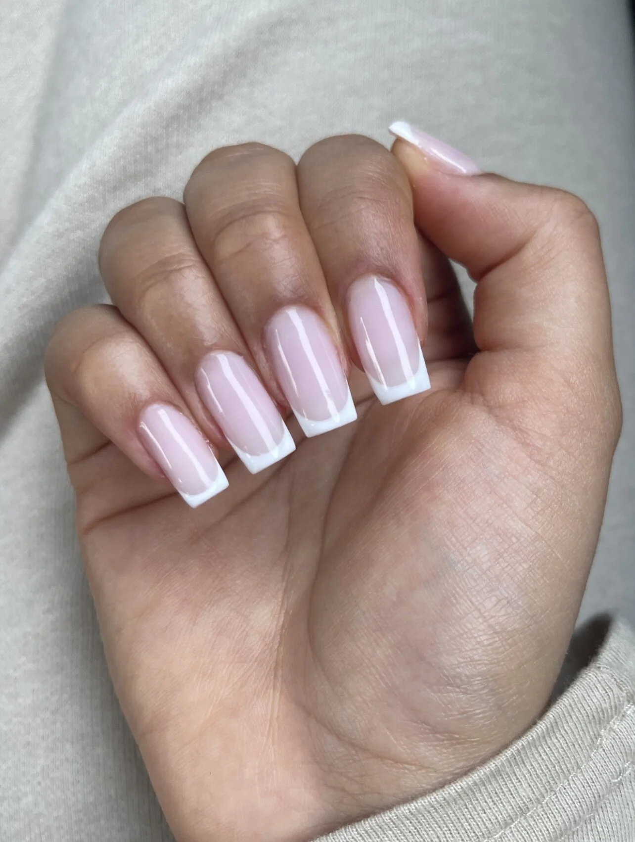 Main avec ongles manucurés en french manicure, tenant une main en forme de poing.
