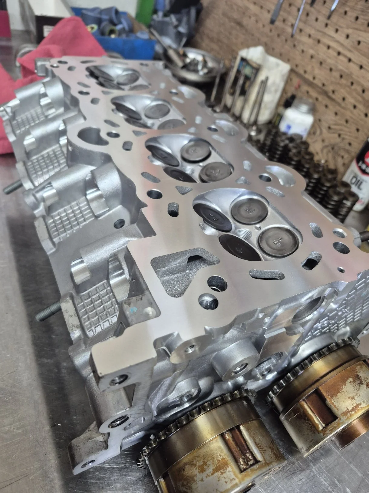 Engine cylinder head with valves and camshafts on a workbench in a garage.