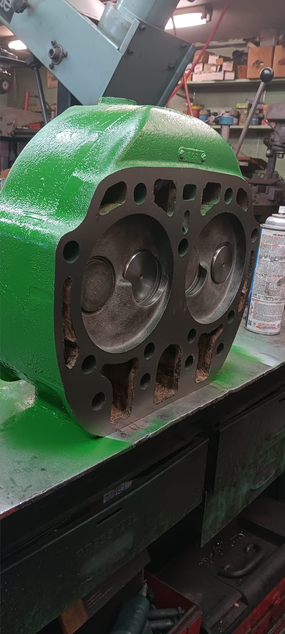 A machined engine block with pistons inside, painted green, on a workbench in a workshop.