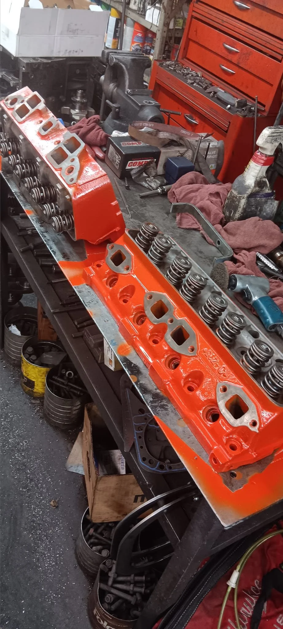 Car valve cover and engine parts on a workbench in a garage or auto repair shop.