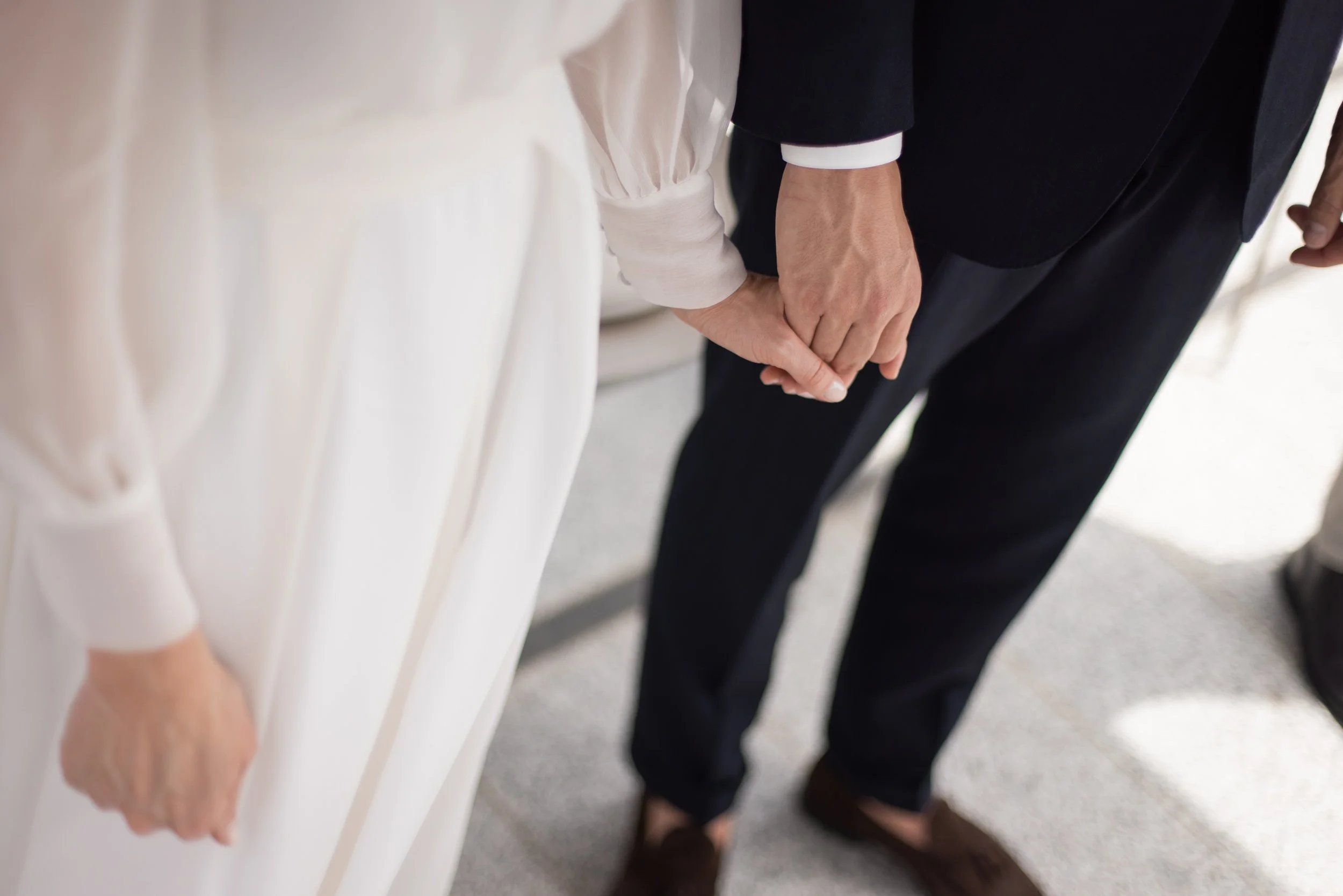 Close-up of a couple holding hands during their wedding ceremony in South Tyrol, with the bride wearing a white dress and the groom in a dark suit.
