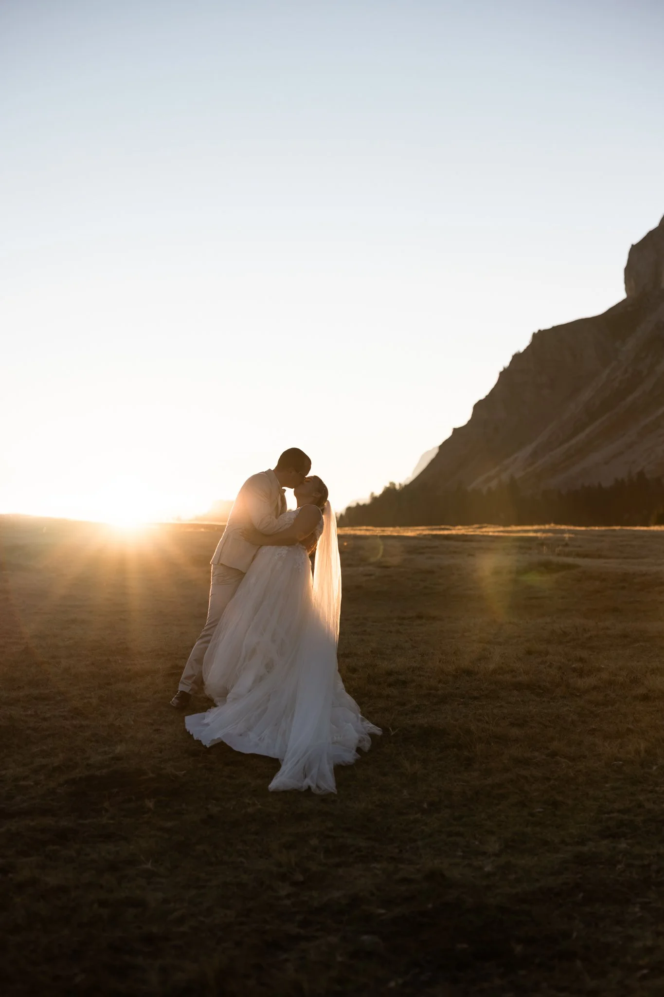 A couple dressed in wedding attire sharing a kiss at sunset on Würzjoch, Passo delle Erbe (Dolomites) with Mount Peitler in the background.