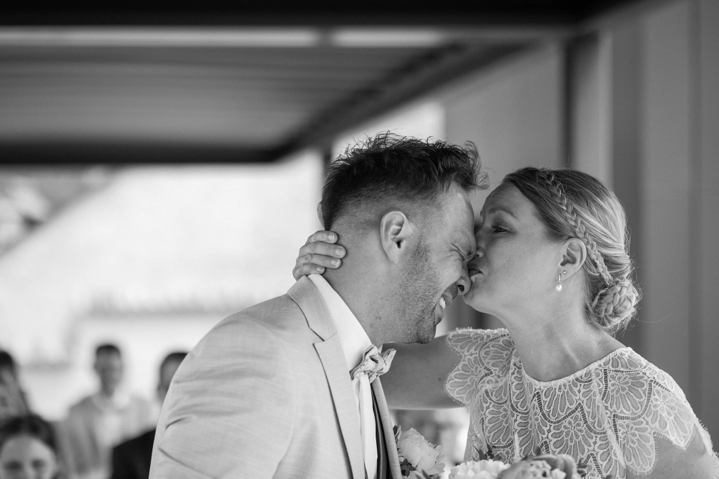 Black and white photo of a bride and groom kissing during their wedding ceremony on the roof top terrace of Brixen, with the bride wearing a lace dress and the groom in a suit.
