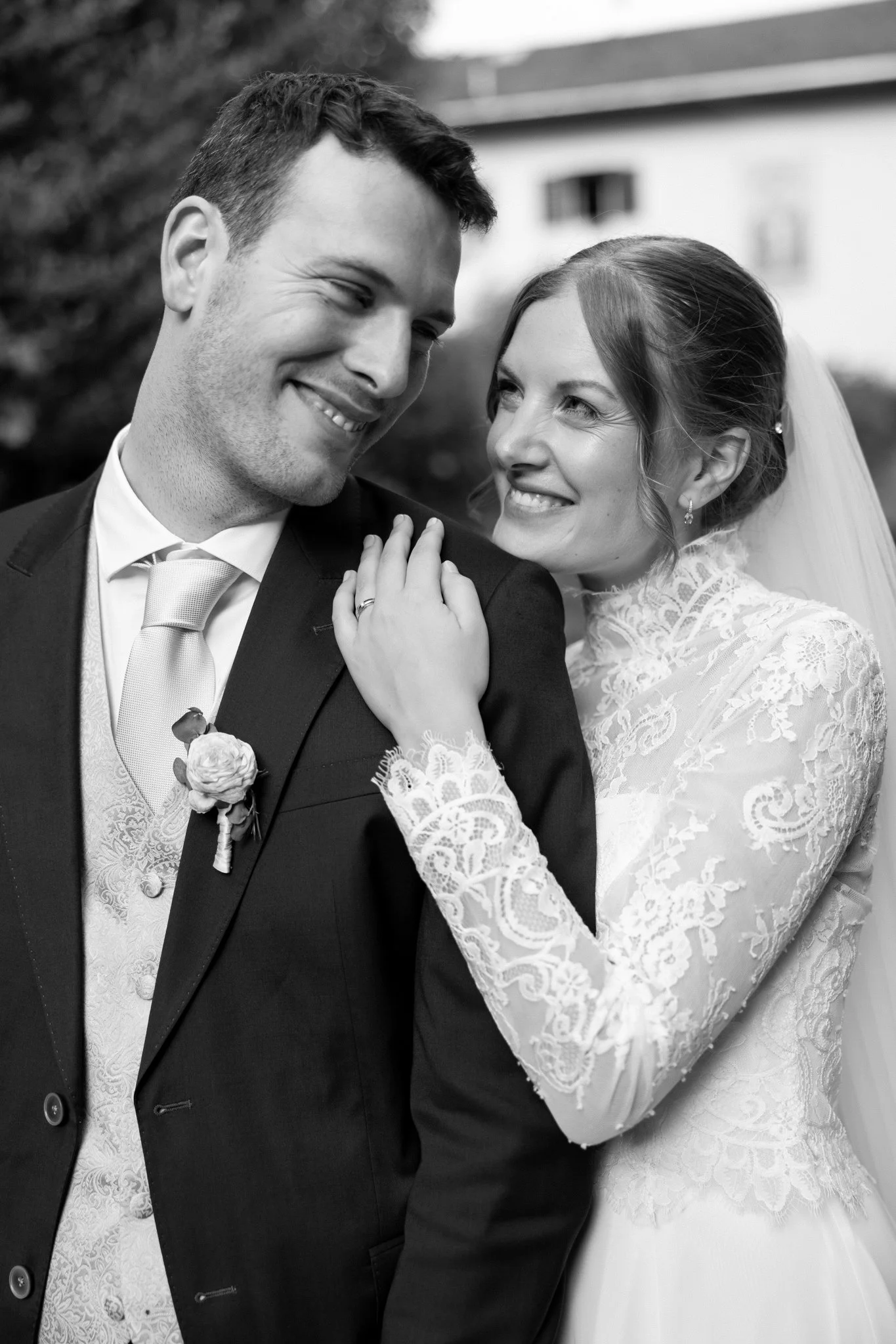 Black and white photo of a bride and groom smiling and looking at each other, with the bride touching the groom's shoulder.