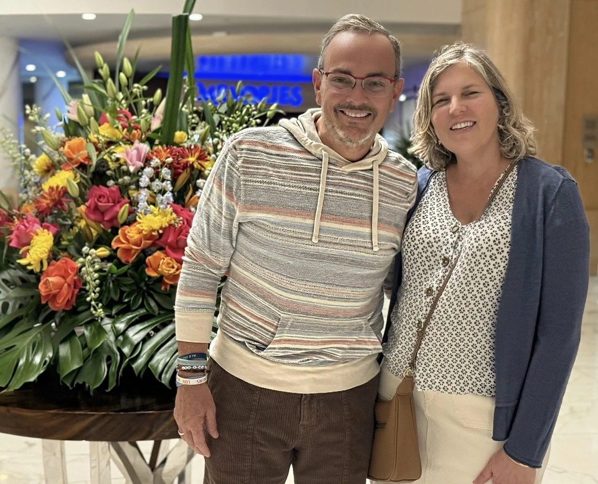 Lisa and Kevin Martin smiling together beside a colorful flower display.