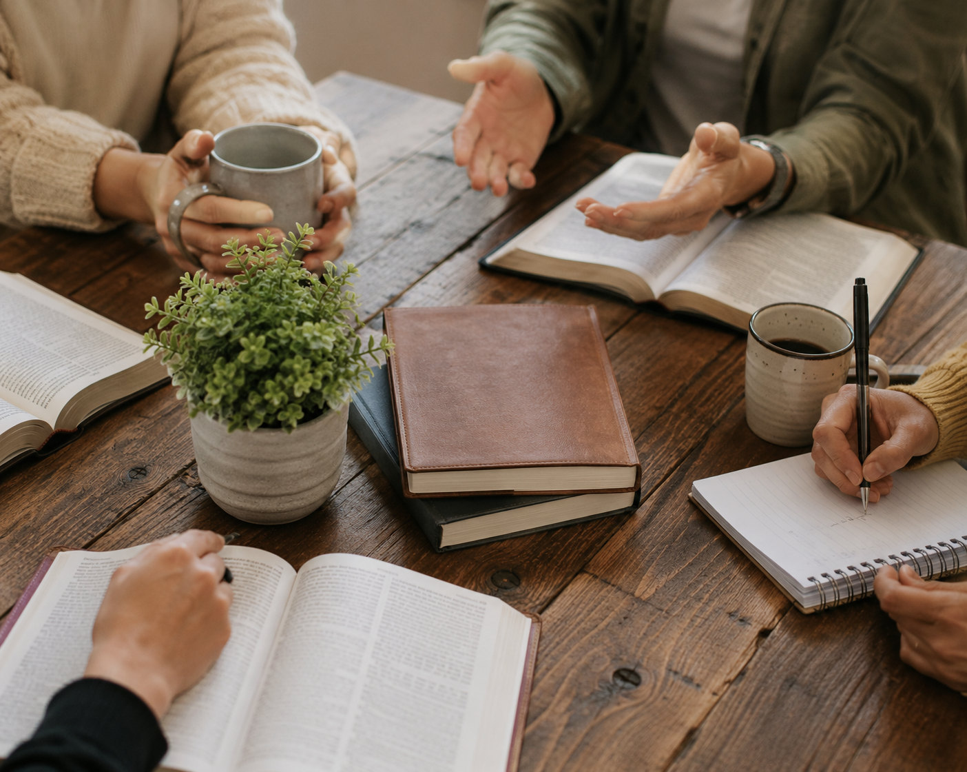 Group of people gathered around a table with books and coffee, reflecting the discussion and community themes in Our Healing Home.