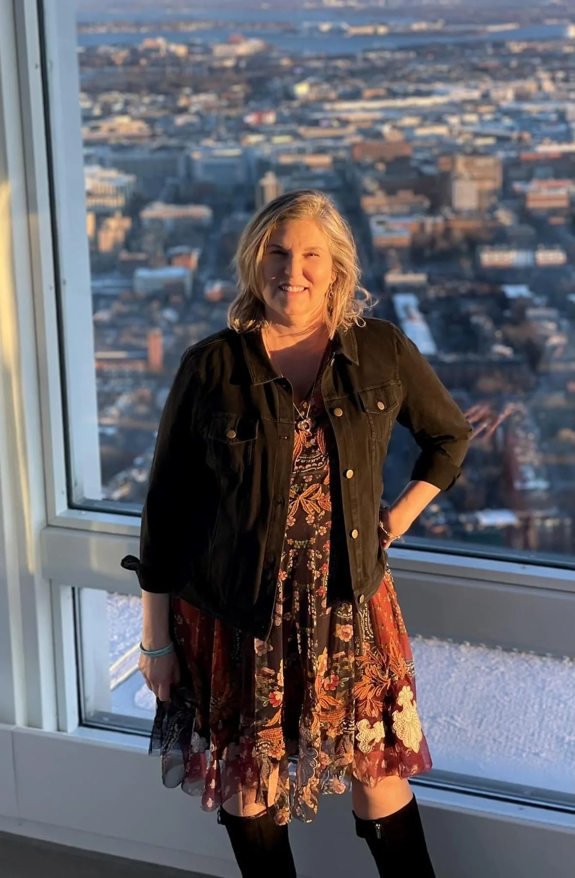 Lisa A. Martin, author of Our Healing Home, standing by a window overlooking the city.