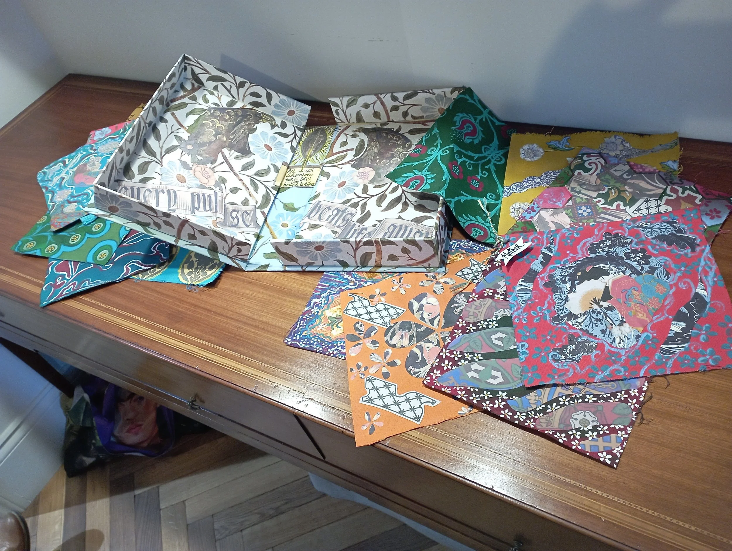 A wooden table with colorful fabric scraps and a large decorative box with a floral and leaf pattern.
