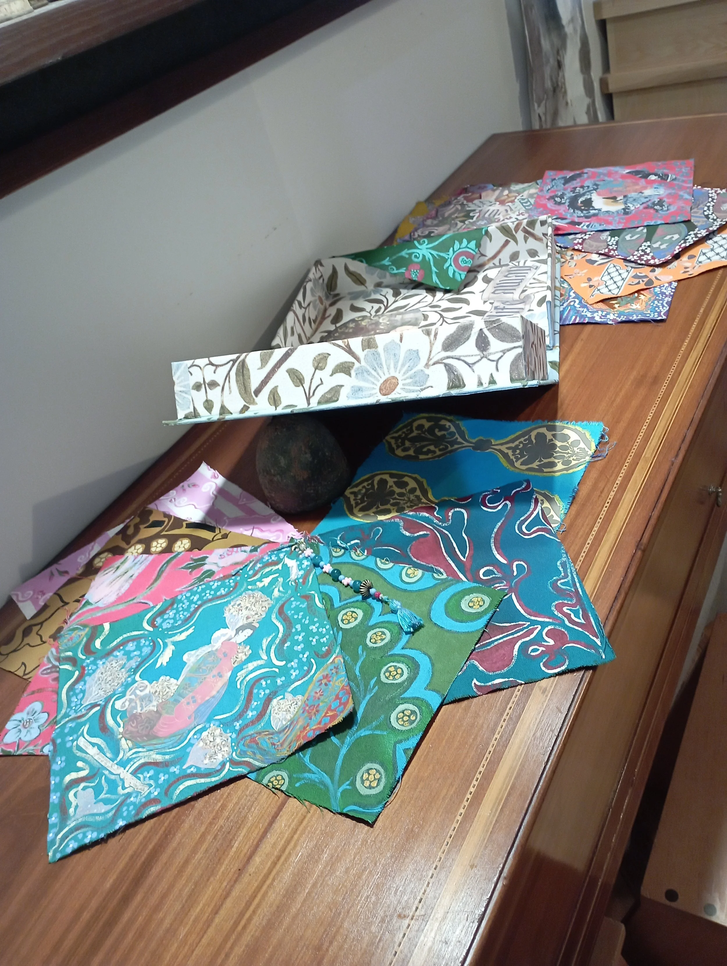 Colorful fabric pieces with various patterns and a large floral box on a wooden table.