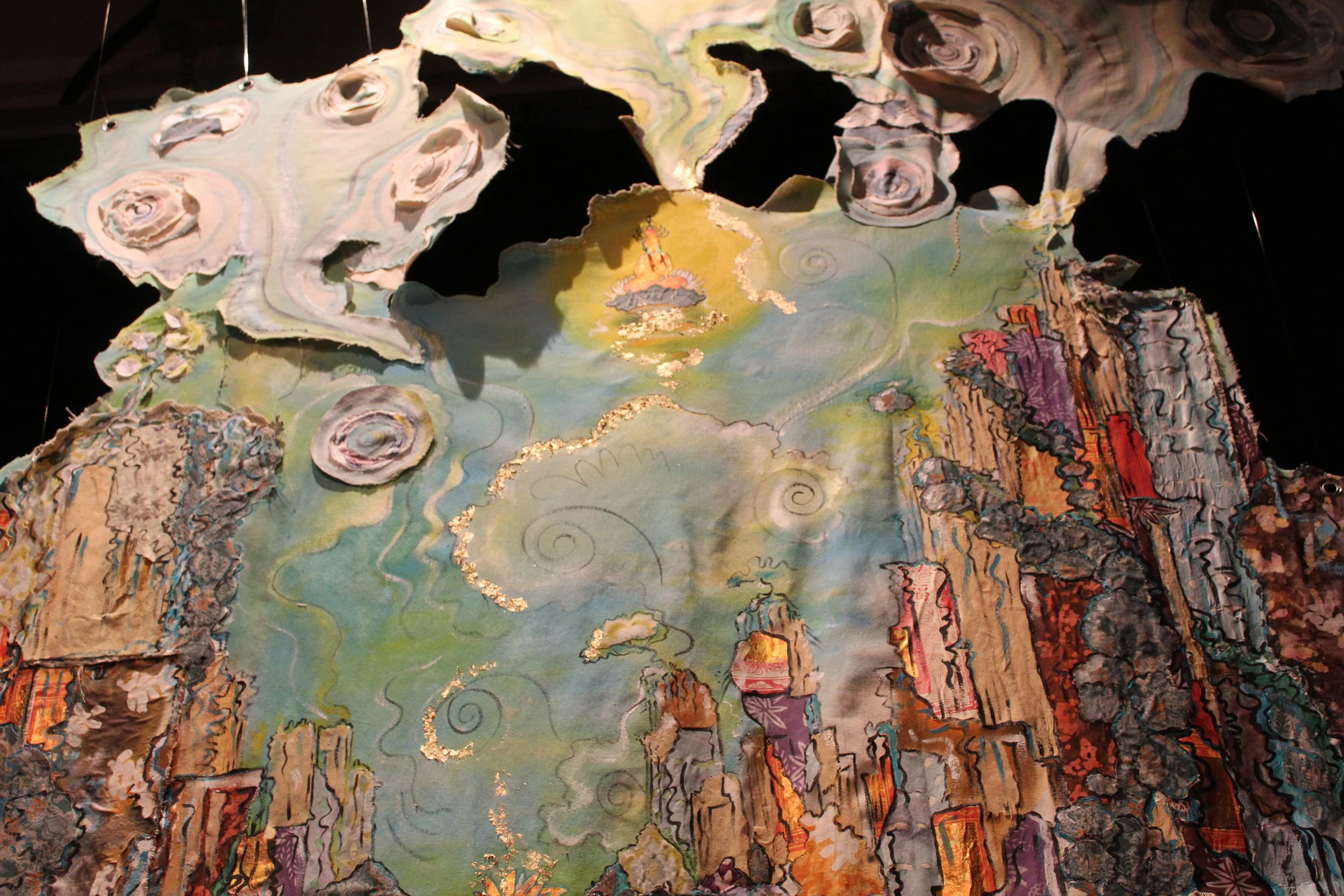 An abstract hanging art piece with cloud-like, swirling shapes, and a landscape featuring tall, colorful rock formations and a small figure sitting near a lake, with delicate gold accents and pastel colors.