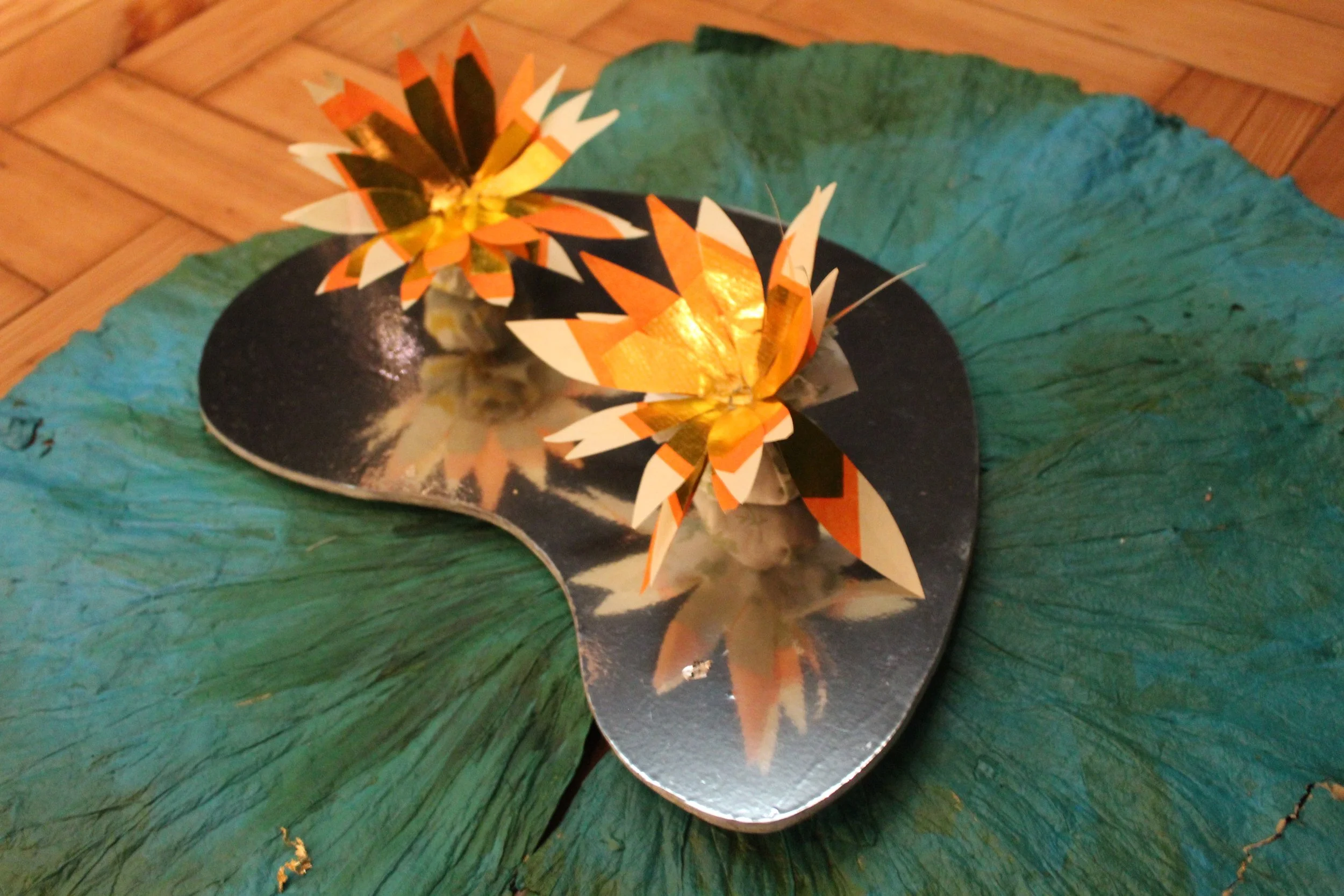 Decorative paper flowers on a mirror placed on a large green leaf.