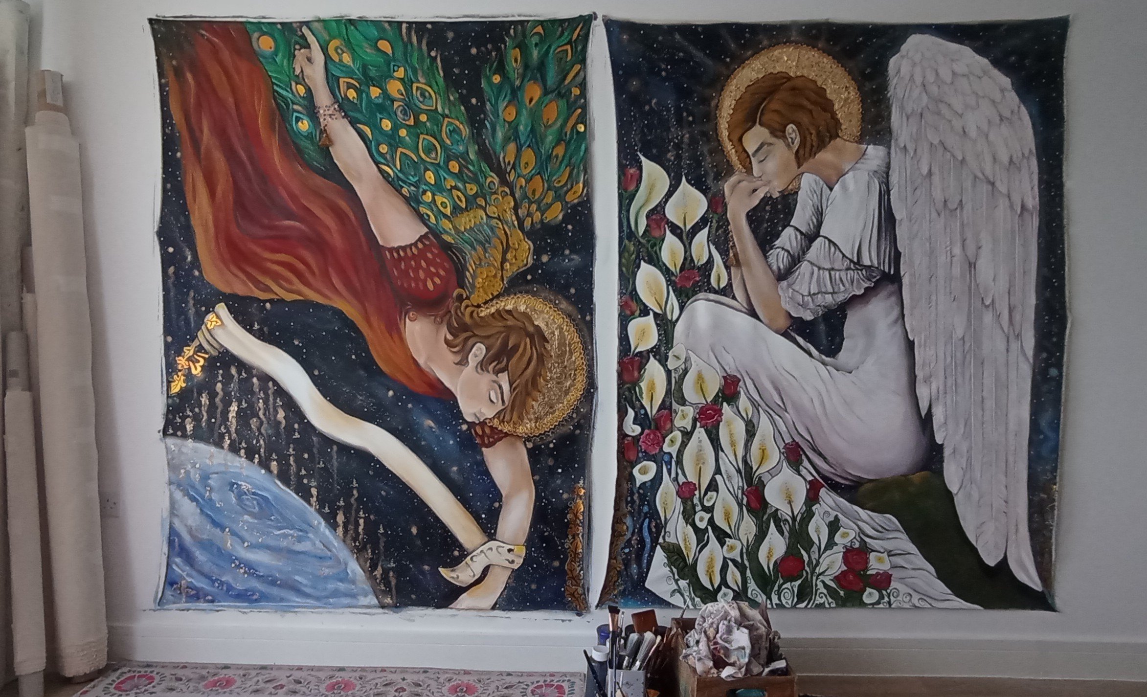 Two paintings on a wall depicting angels. The left angel has long reddish hair, a golden halo, and is reaching toward a globe with a starry background. The right angel has short brown hair, white wings, a golden halo, and is sitting with eyes closed,