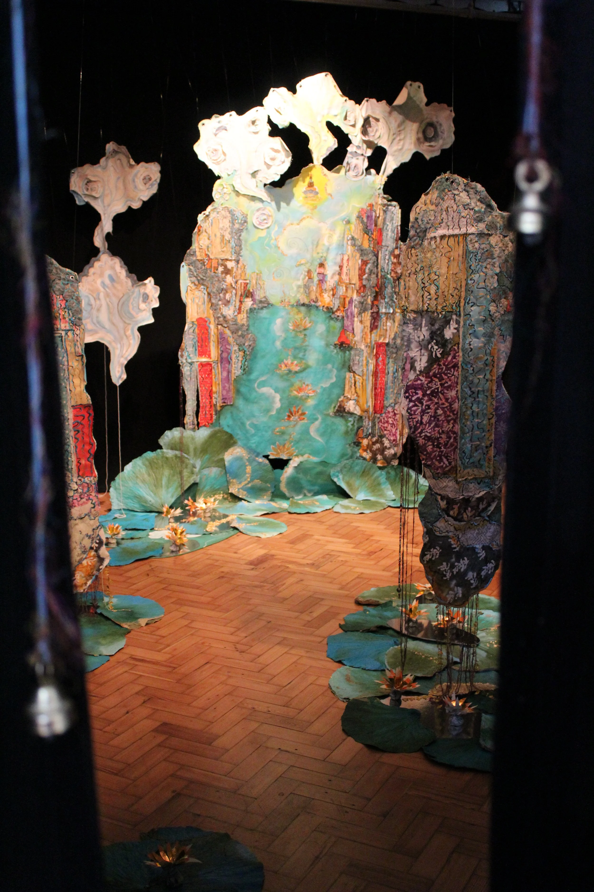 Colorful artistic installation resembling a landscape with water lilies, water, mountains, and clouds, viewed through a doorway.