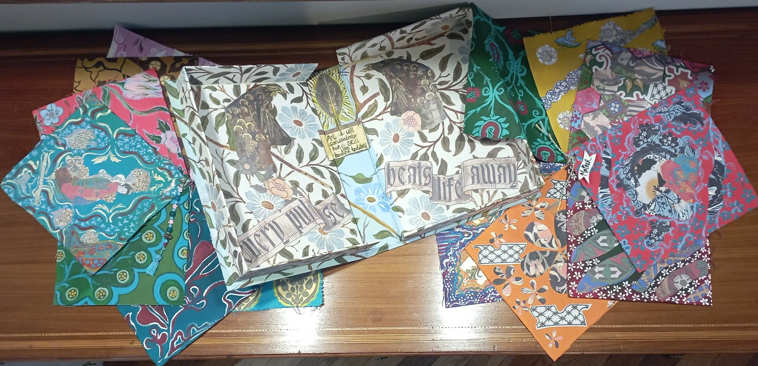 A collection of colorful bandanas with various patterns and designs, spread out on a wooden surface. In the center, there is a book titled 'Beast Life' with a floral and animal-themed cover.