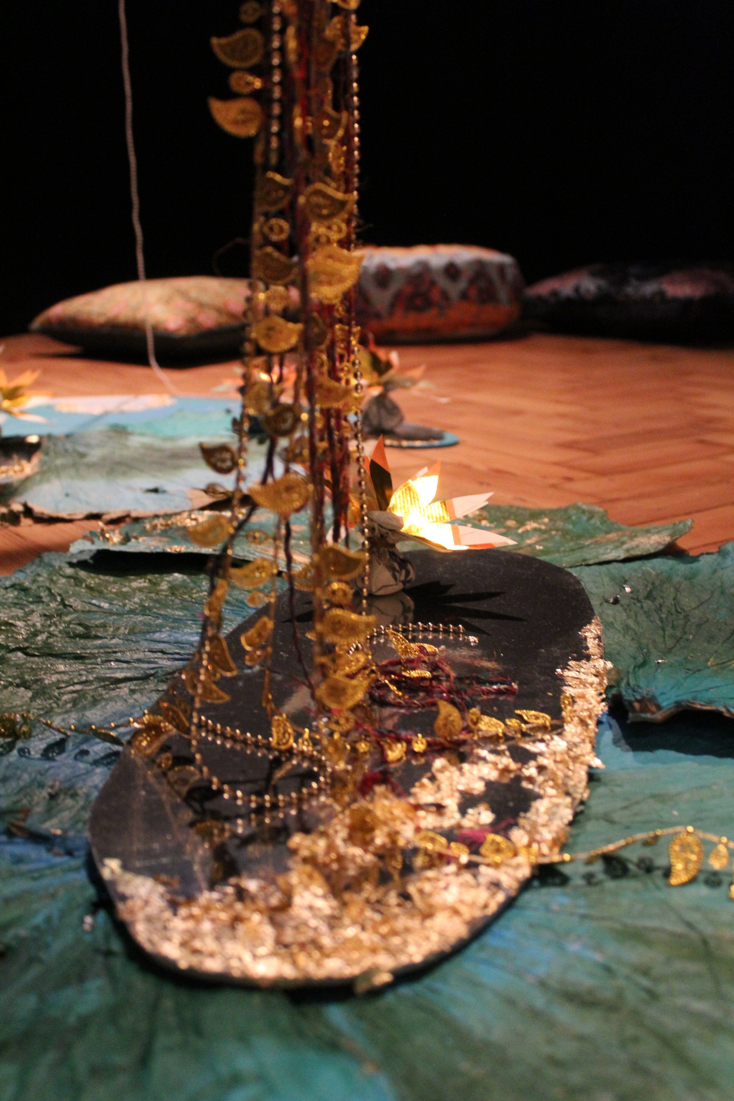 Close-up of a gold jewelry display on a decorated surface with cushions and pillows in the background, dim lighting.