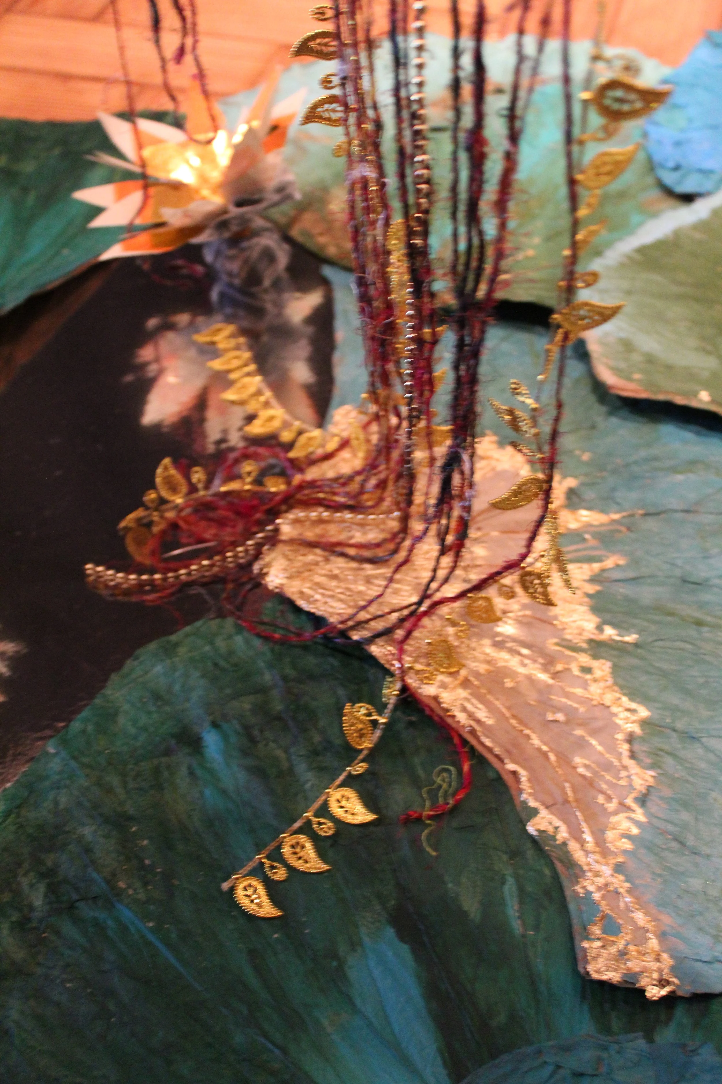 Close-up of a collection of textile and jewelry items, including embroidered fabric, strings of beads, and gold-colored leaf-shaped decorative elements.