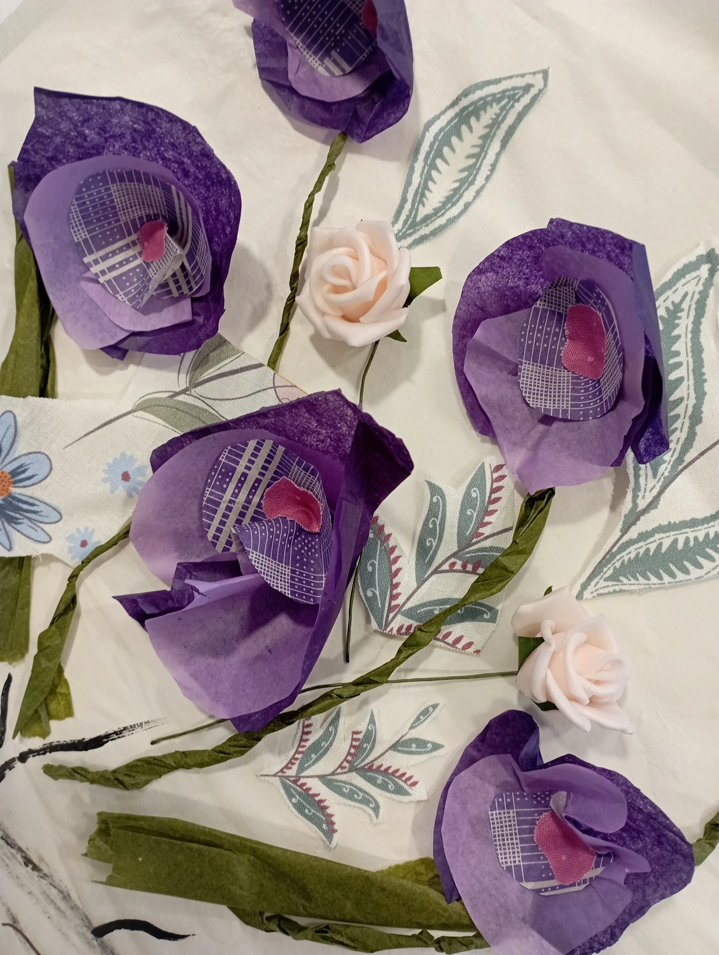 An arrangement of purple and cream paper flowers with printed leaves on a white surface.