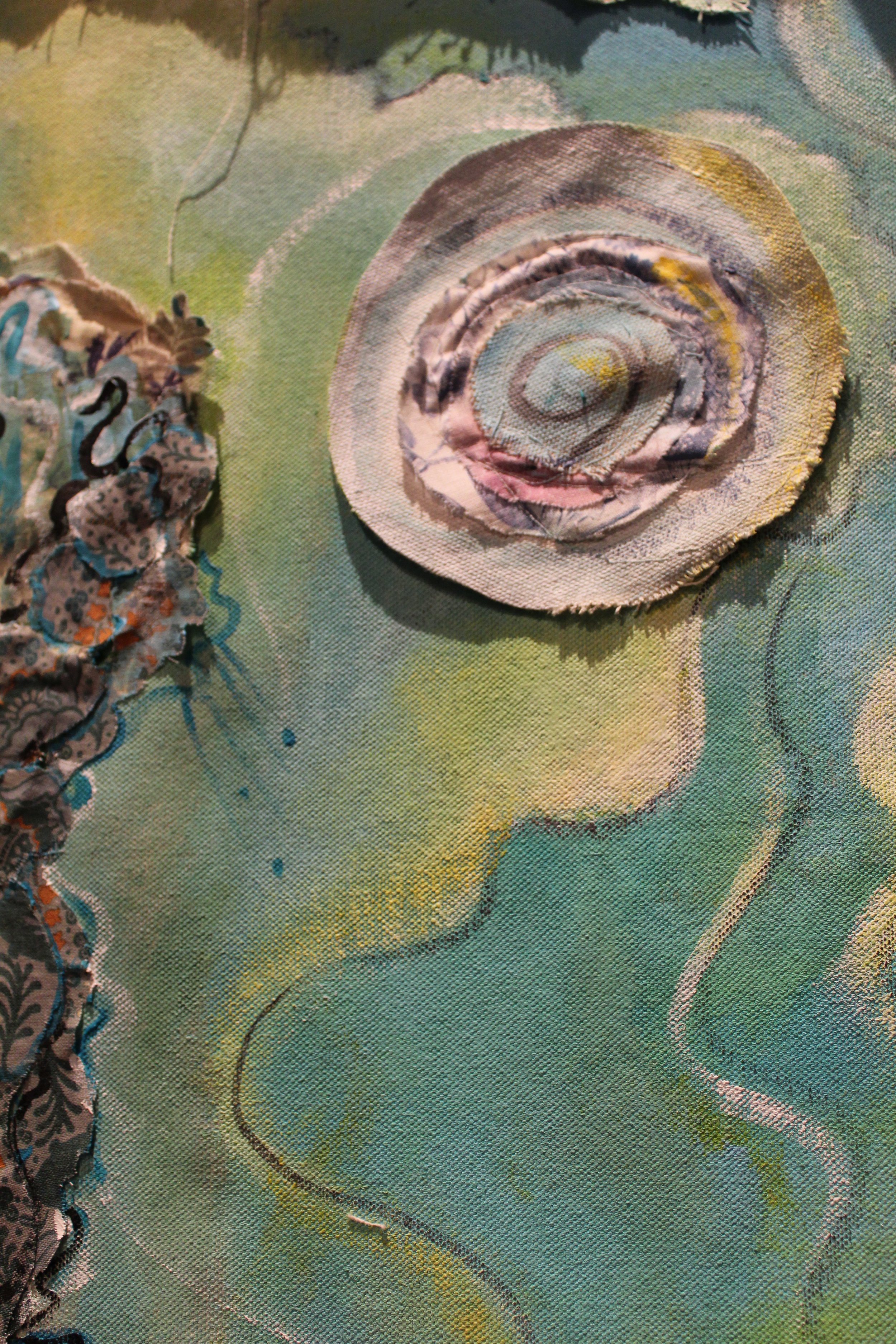 Close-up of fabric art with layered, textured spiral shell and abstract face outline painted on fabric.