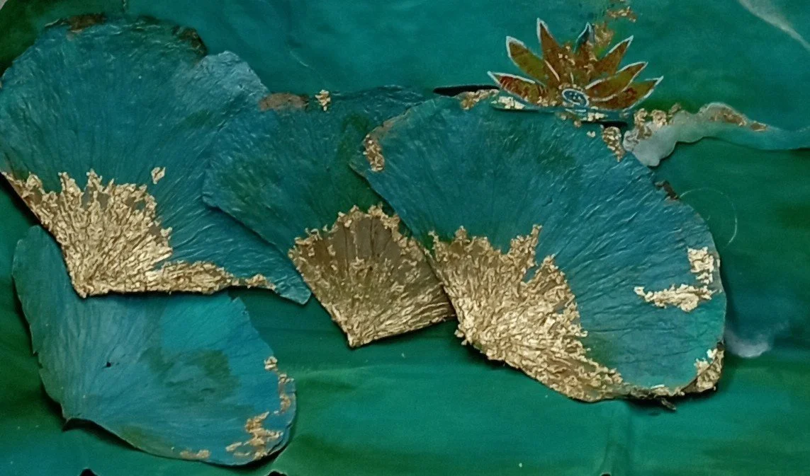 Green and gold decorative leaves, possibly made of paper or fabric, arranged on a surface.