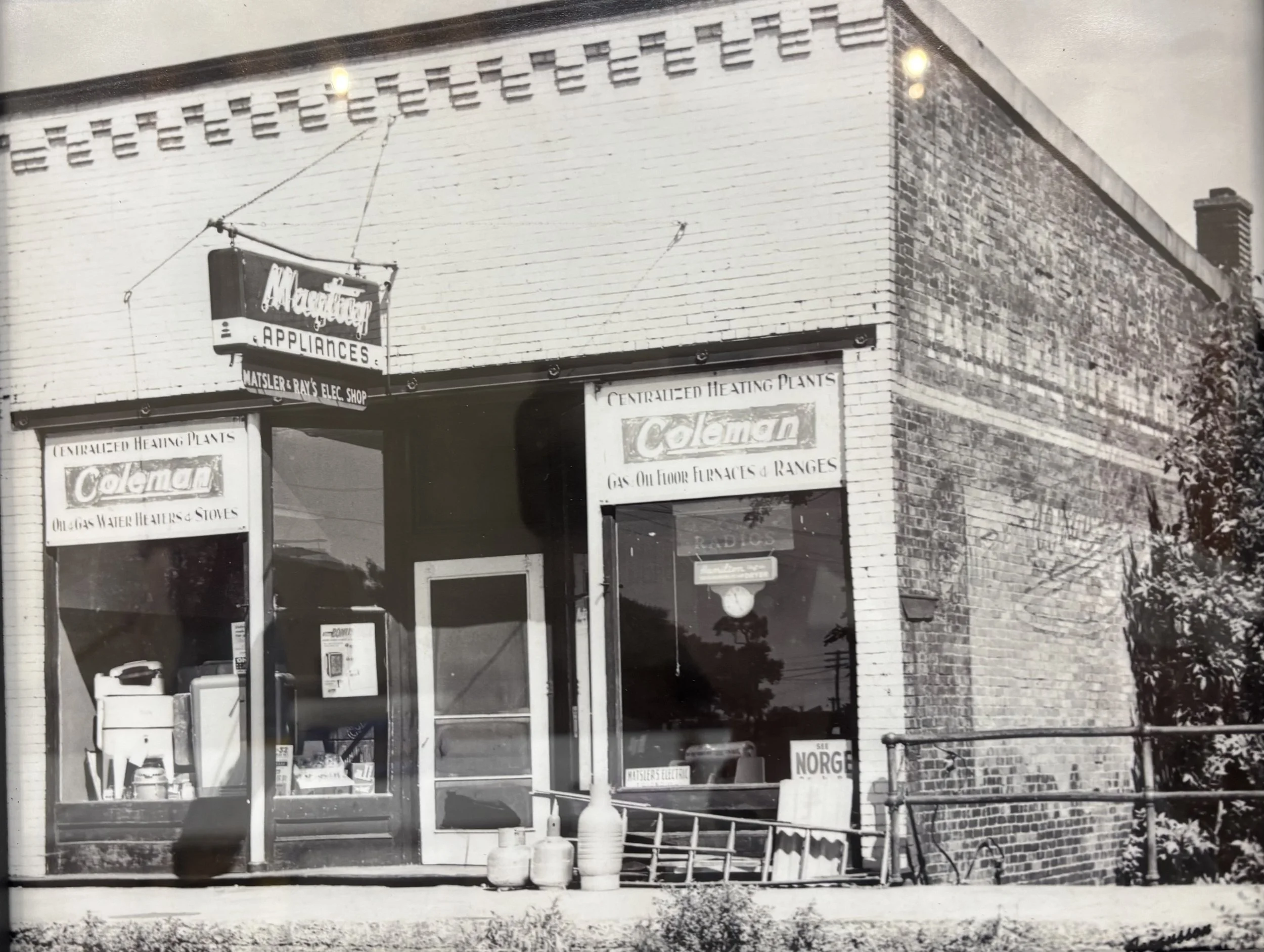 Black and white photograph of a storefront for Matzler & Ray's Appliance and Electric Shop in Tolono, IL that is now Events at 108 space.