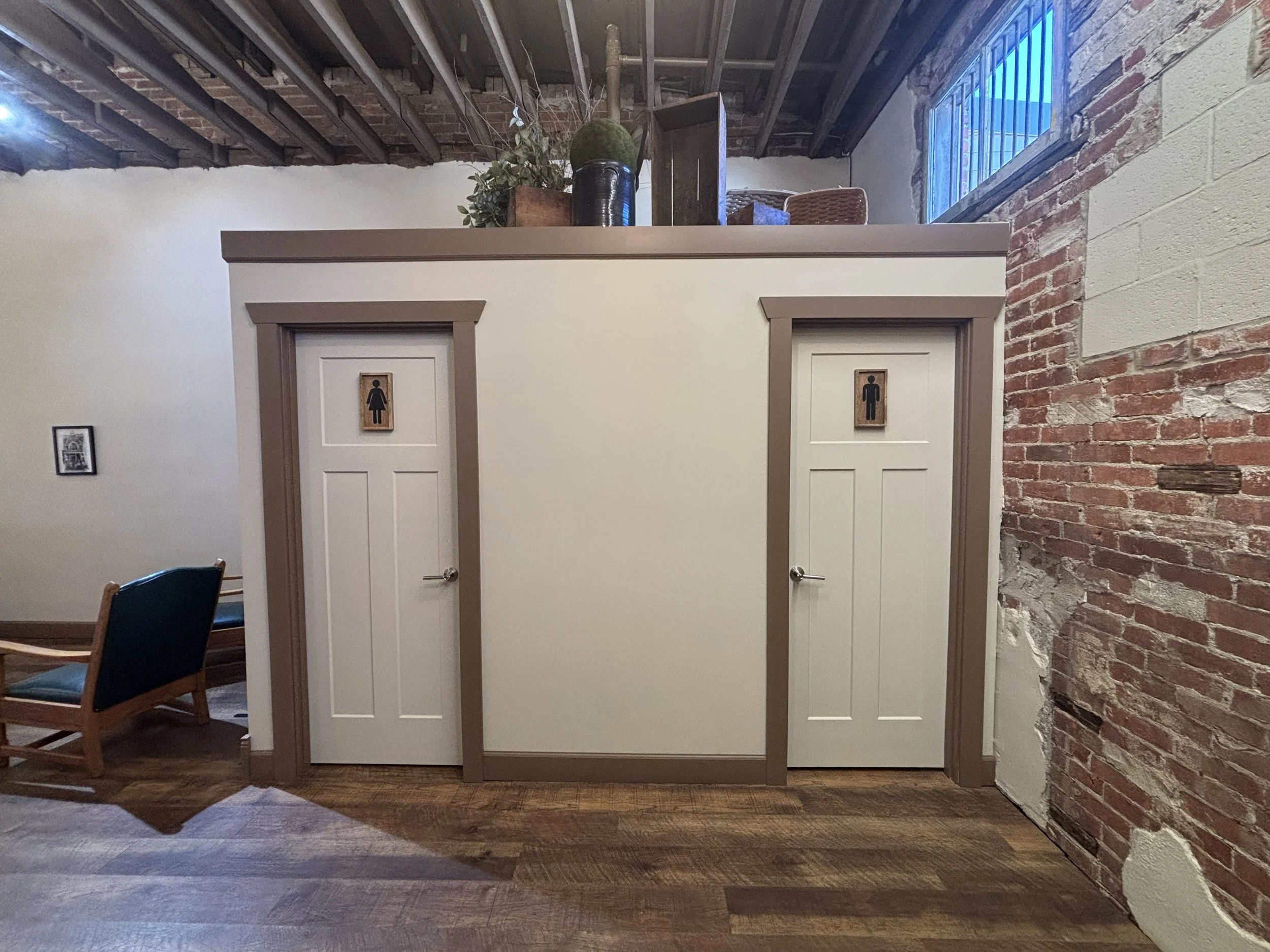 Restrooms with signage on doors, one for women and one for men, inside a rustic-style building with exposed brick walls and wooden flooring.