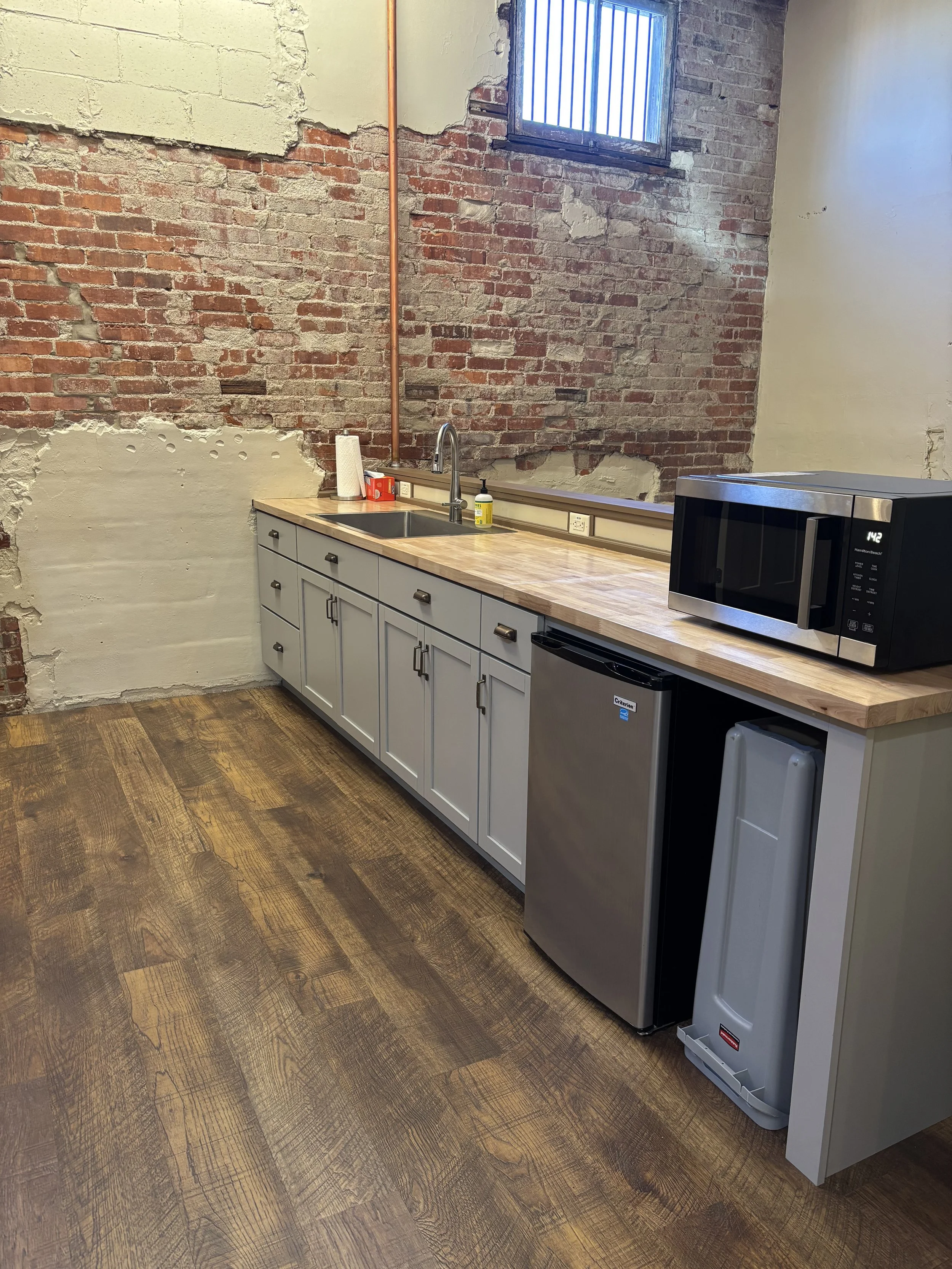 Industrial-style kitchen with exposed brick wall, white cabinetry, a wooden countertop, a microwave, and a mini fridge.