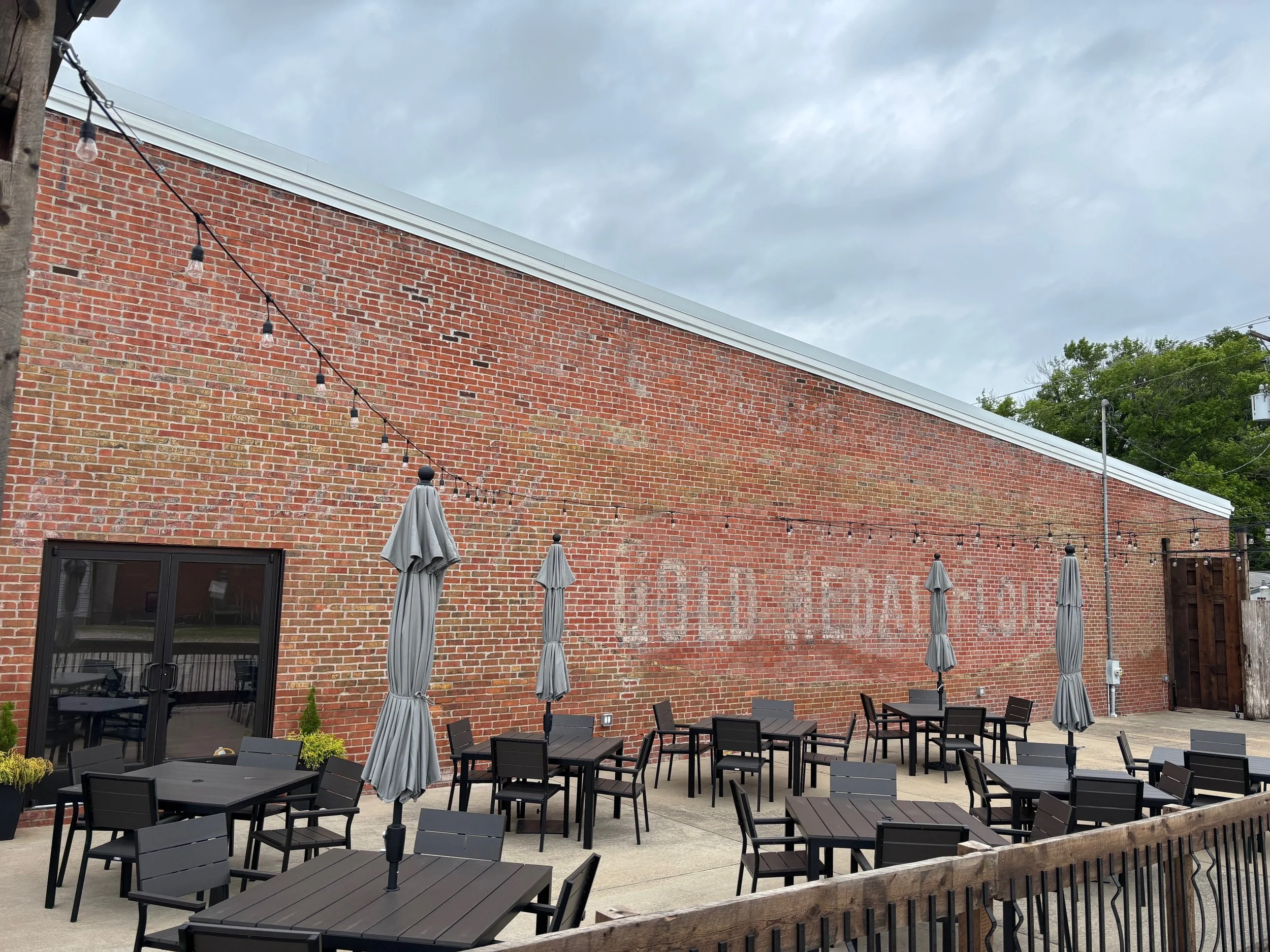 Outdoor patio with black tables and chairs, gray umbrellas, string lights, against a brick wall with faded painted sign that reads 'SOUTHERN KITCHEN' and a sliding glass door.