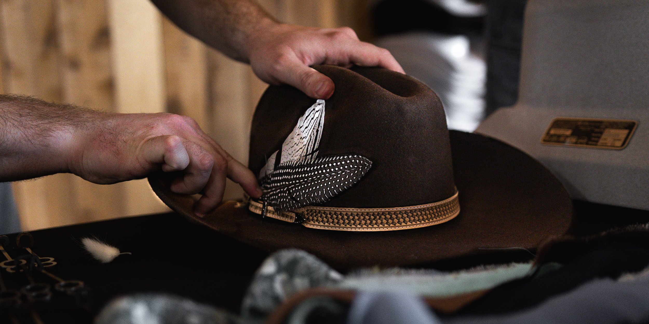 Hands placing a decorative feathered hat on a table.