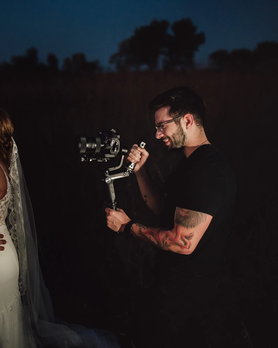 Photographer using a camera stabilizer to shoot a woman in a white dress outdoors at night.