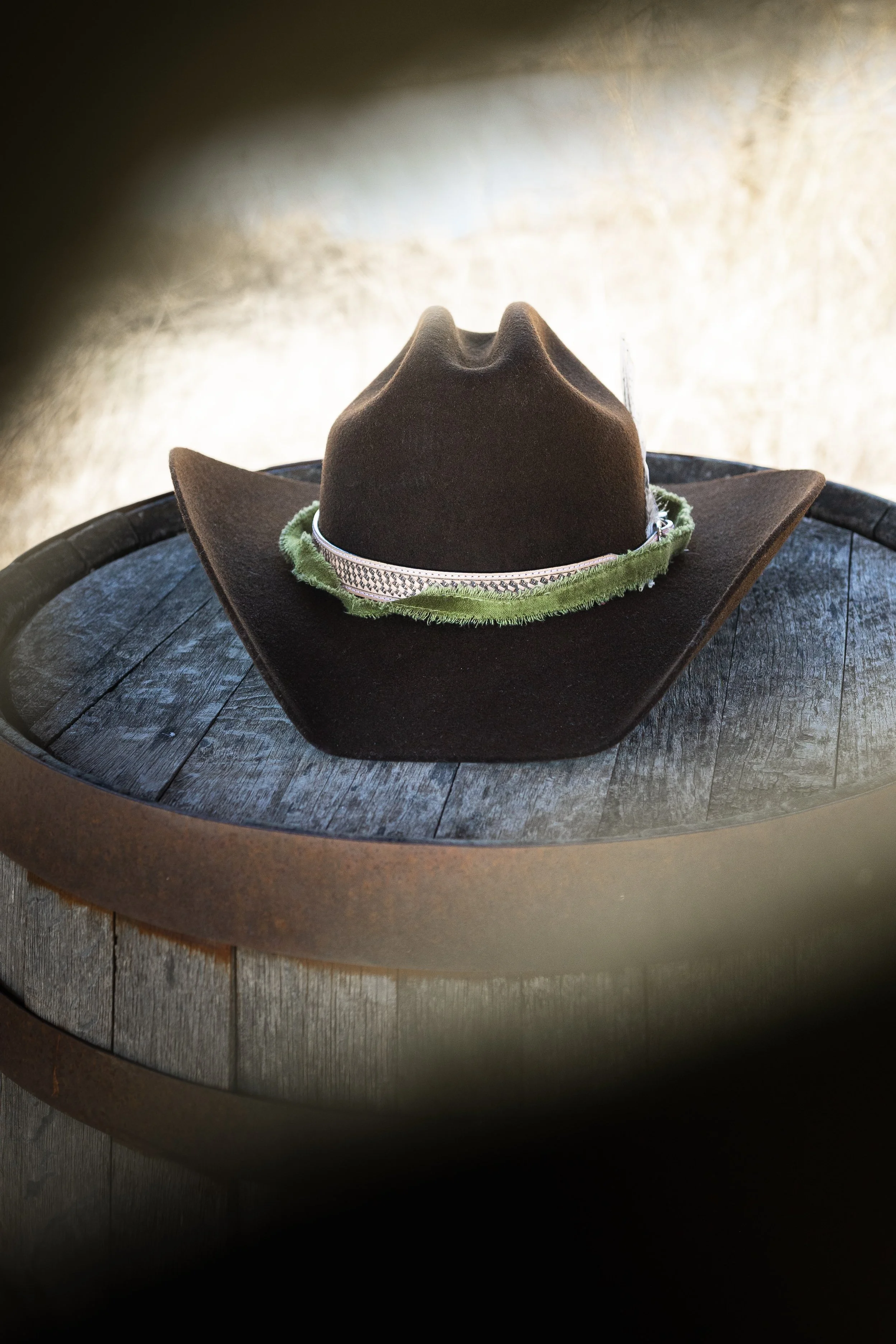 A brown cowboy hat with a decorative band, placed on a dark wooden barrel.