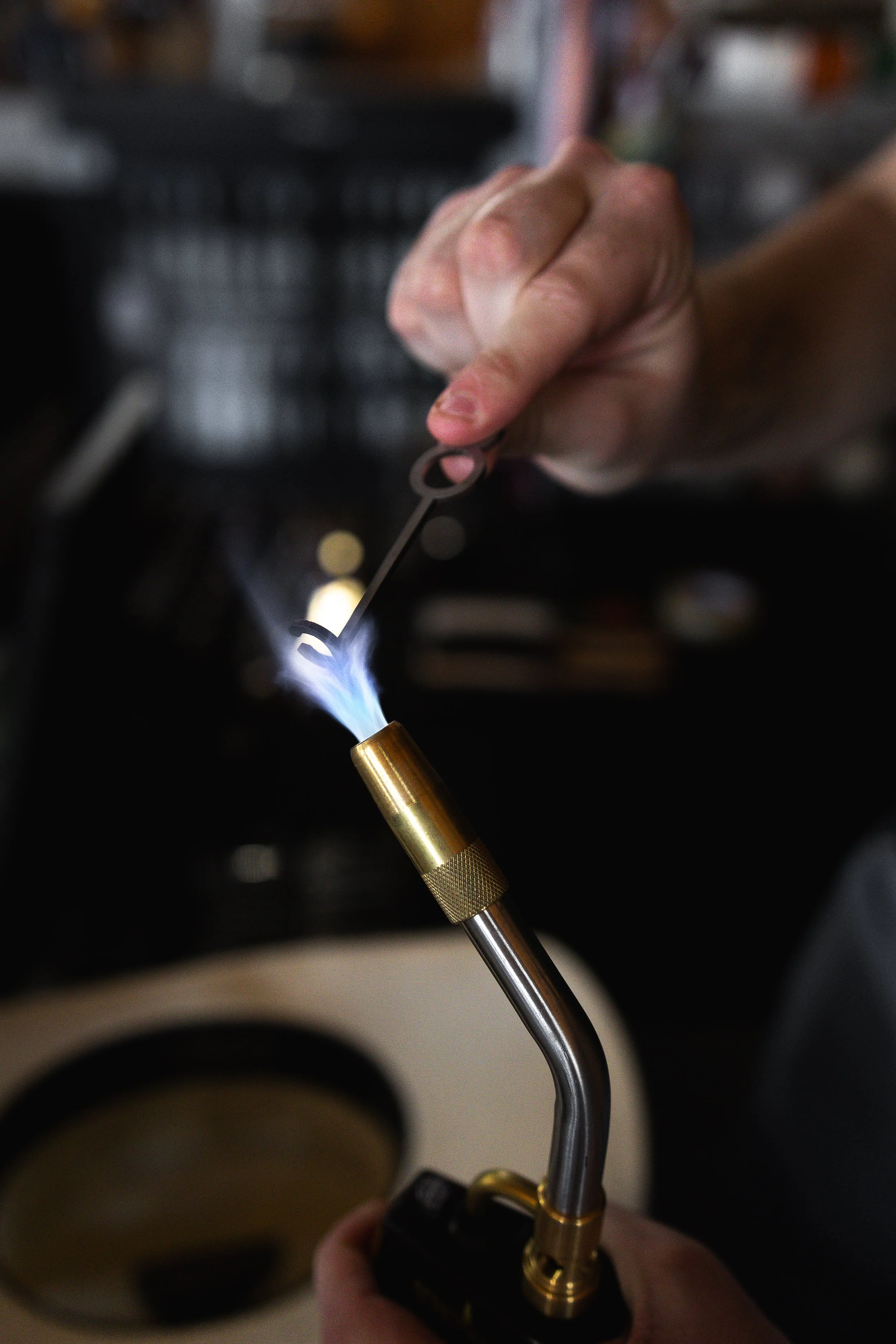A hand holding a blowtorch with a blue flame, igniting a metal object.