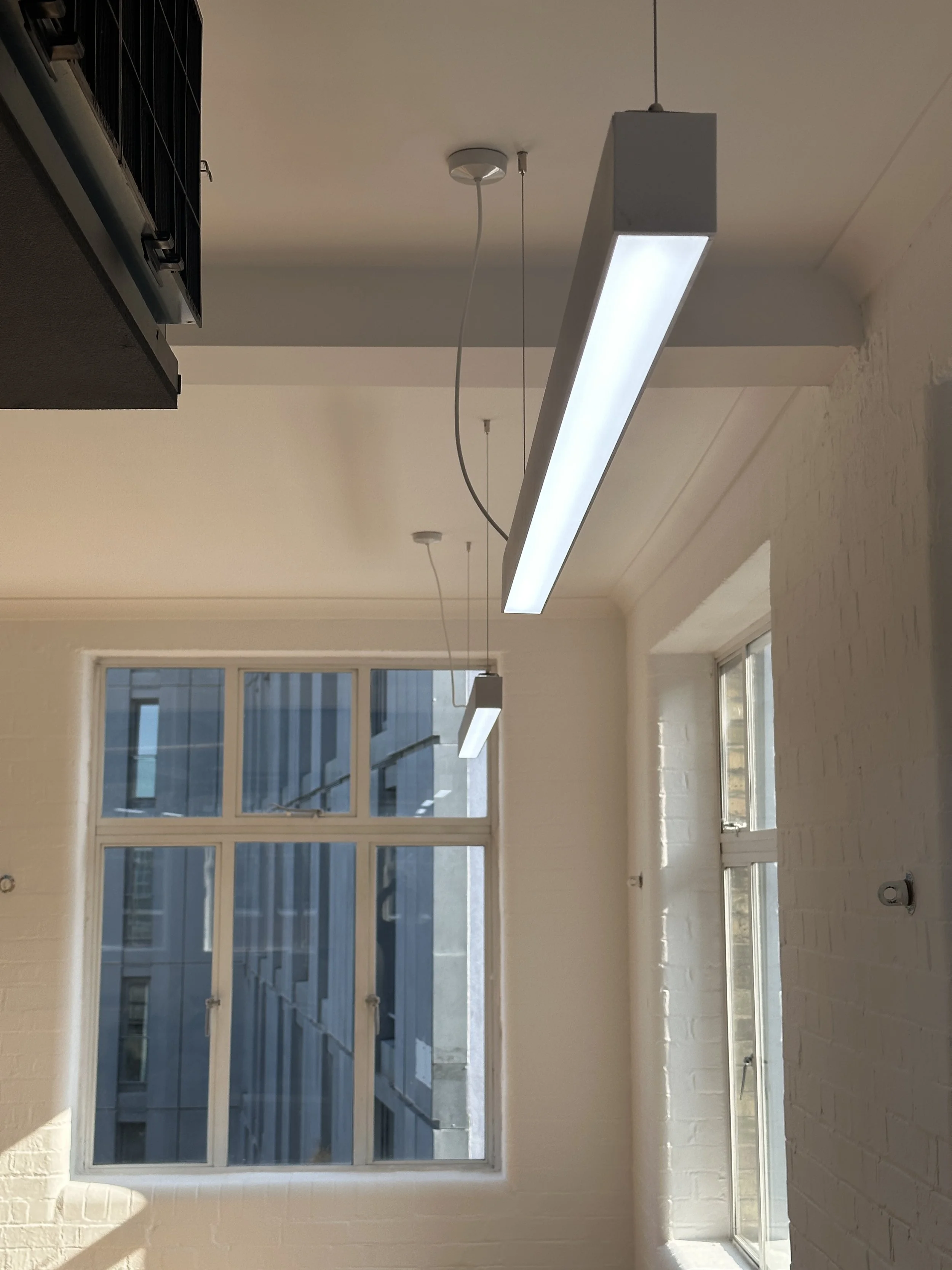 Empty room with large window, white brick wall, and ceiling lights.