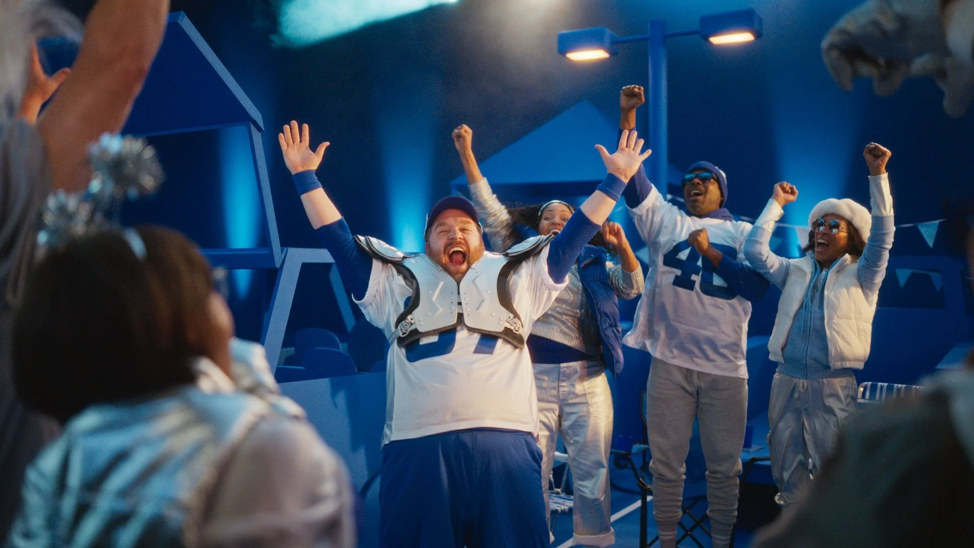 Group of football players celebrating on the sidelines, cheering with their arms raised in victory.