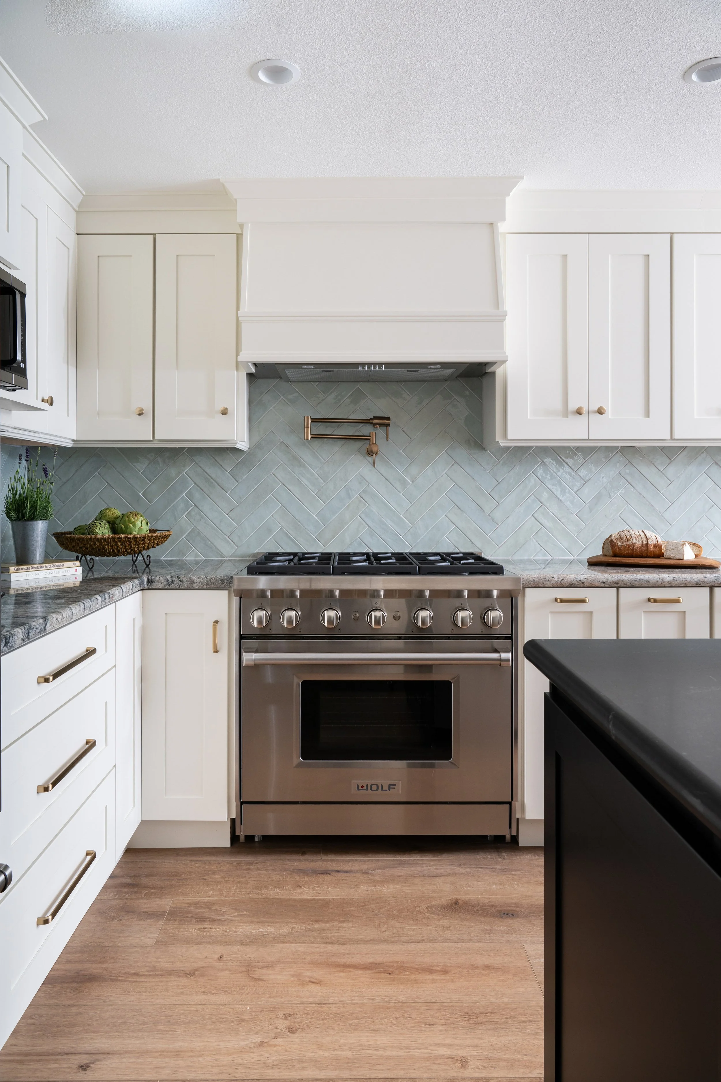 A modern kitchen with white cabinets, a stainless steel Wolf oven, a herringbone tile backsplash, and a wooden countertop with a loaf of bread on a cutting board.