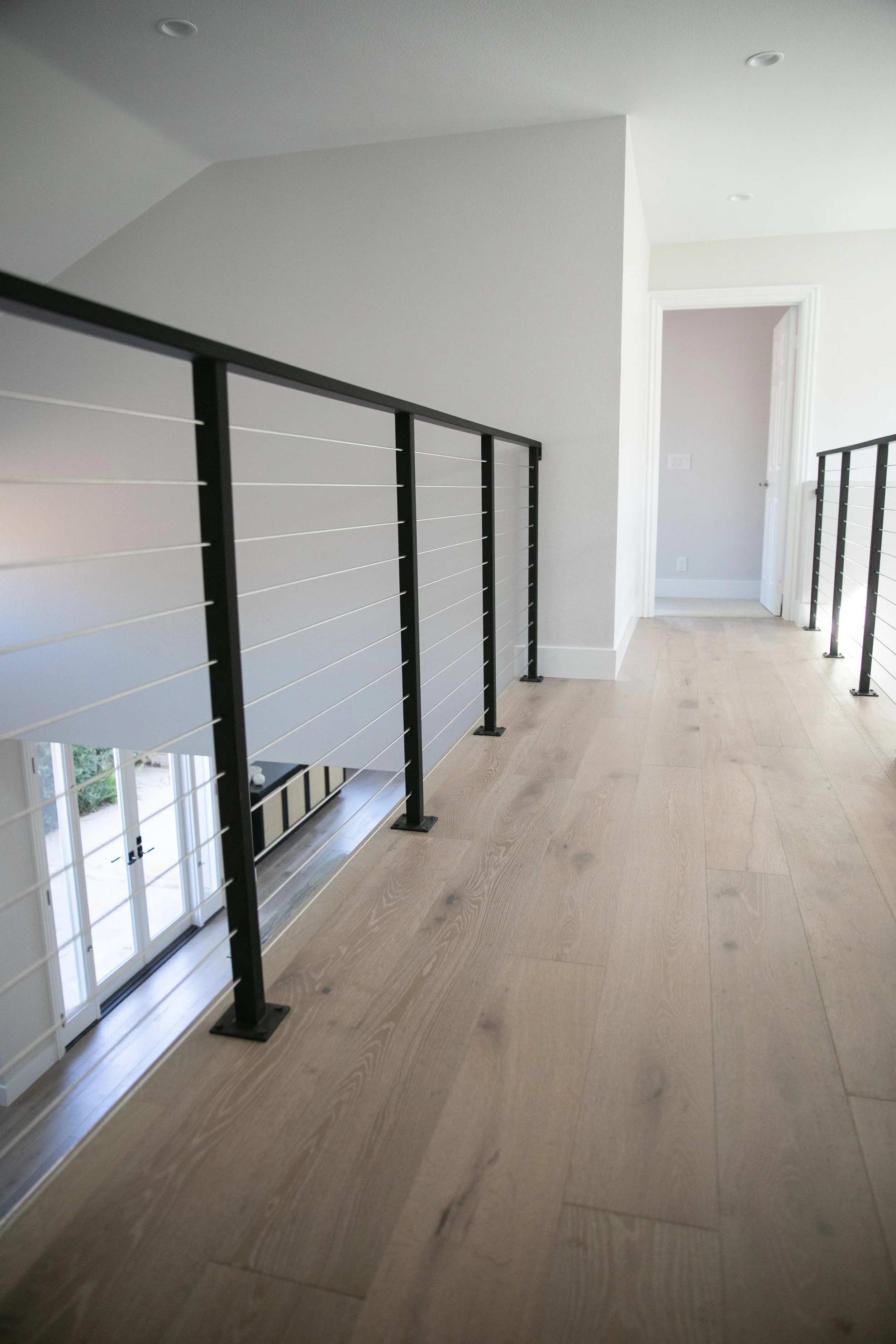 Redesigned and newly constructed open concept hallway with openwork metal stair railing, white oak floors, and soft gray walls.