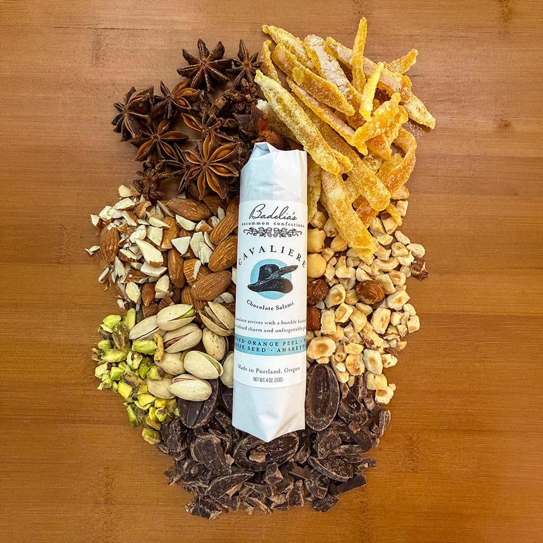 Cavaliere flavor of chocolate salami wrapped in white butcher paper and labelled with key ingredients like candied orange peel, nuts, anise seed, and chocolate.surrounding the product.