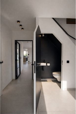 View of a modern bathroom with a black and white color scheme, visible through a partial wall, with a sink and toilet inside, and a hallway leading to other rooms.