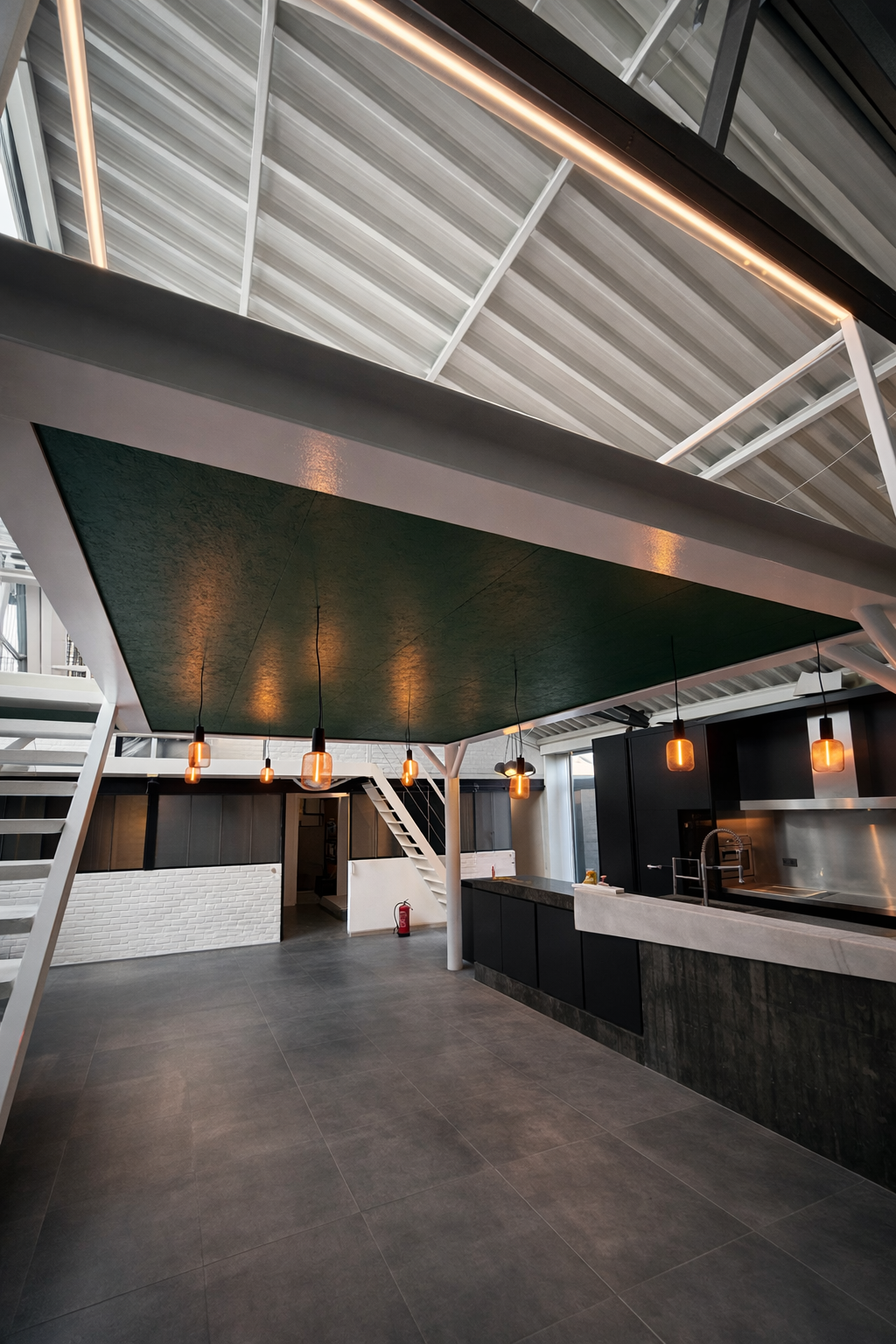 Modern interior of a building with black kitchen counters, warm pendant lights, and an open ceiling with metal beams.