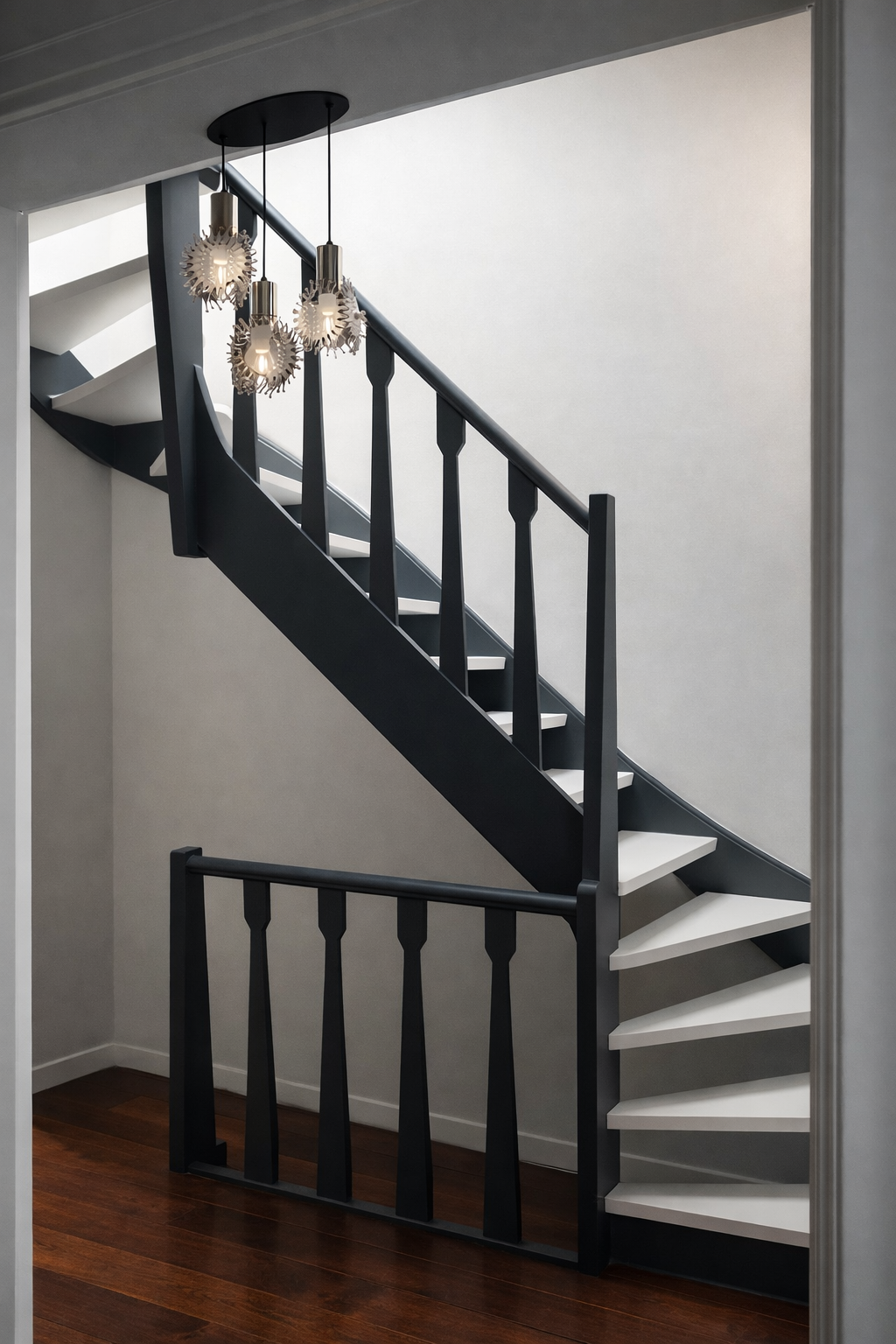 Interior staircase with black railing and white steps, with a modern chandelier hanging overhead, against light-colored walls and hardwood floor.