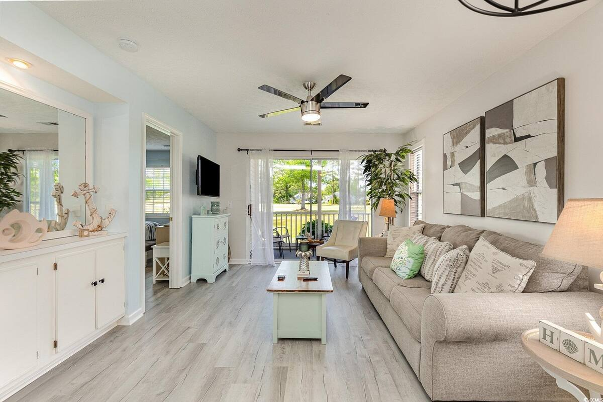 Bright living room in a Myrtle Beach SC rental condo at Waterway Village with large sofa, natural light, and porch view overlooking green lawn.